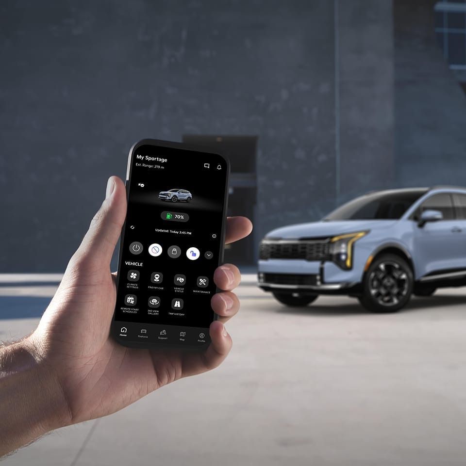 A hand holds a smartphone displaying a car app, with a blue SUV parked in the background.