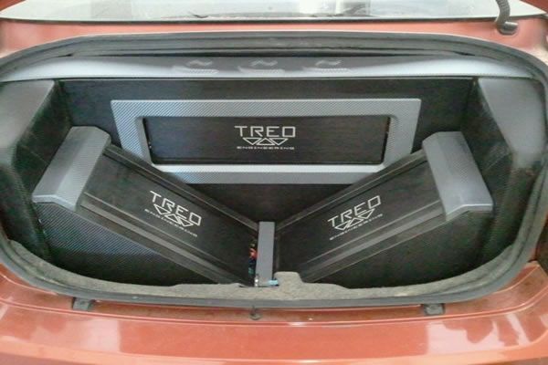Car trunk with two black amplifiers angled towards each other, a gray framed box above them, all with 
