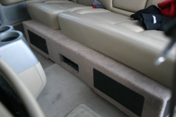 Beige car interior with a custom speaker box built under the back seat. Black speaker covers are visible on the box.