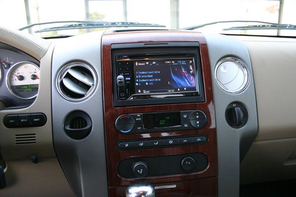 Interior view of a car dashboard with a replaced touchscreen radio, woodgrain trim, and silver accents.
