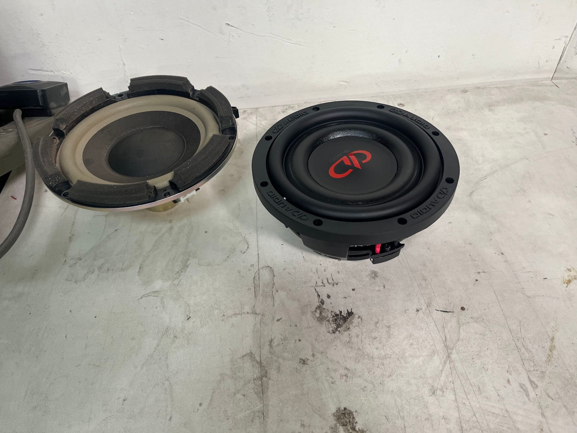 Two black car subwoofers, one disassembled. The newer one with red 