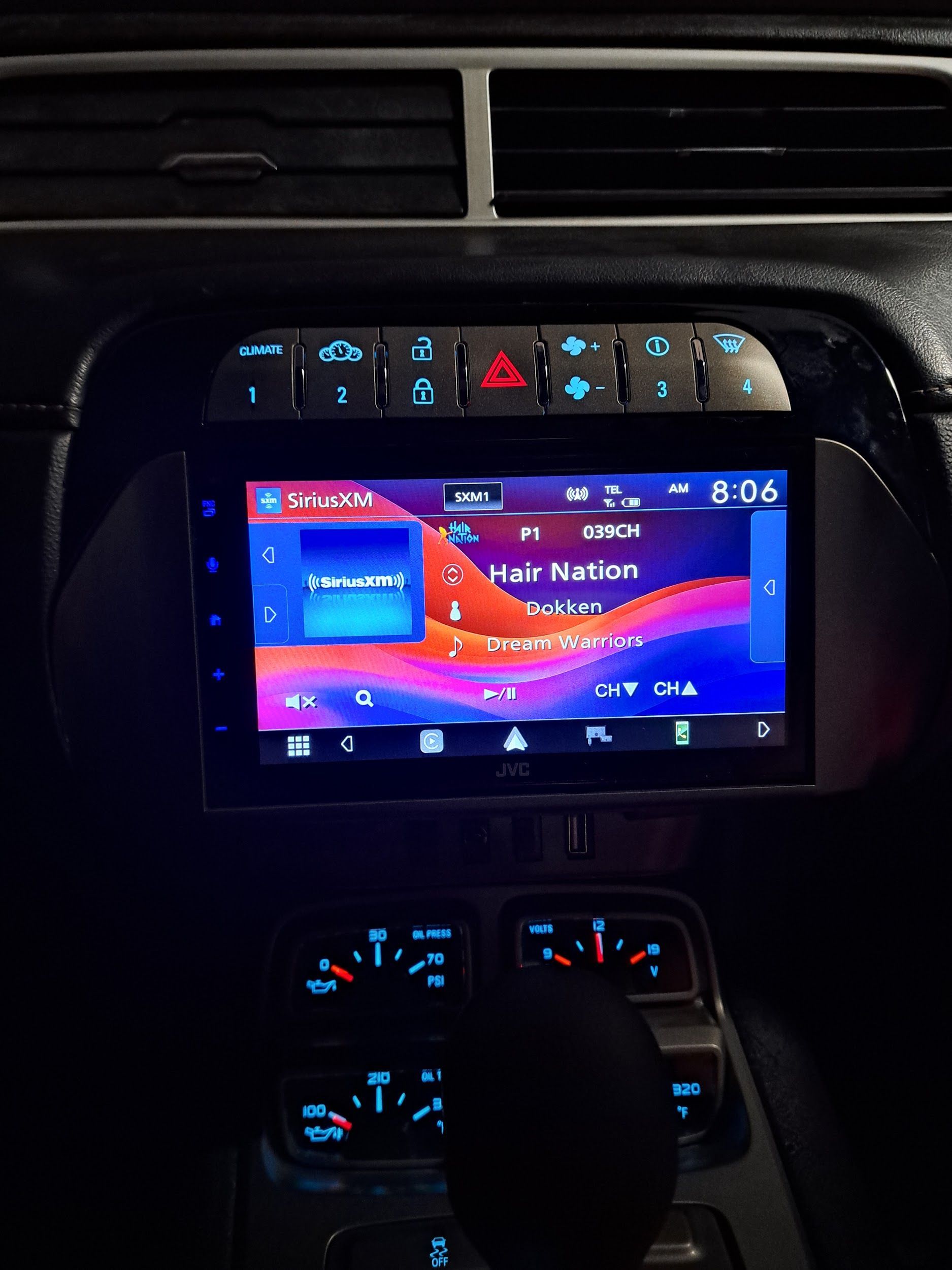 Car's dashboard with a digital display showing music playing. Blue and pink colors. Other buttons and gauges visible.