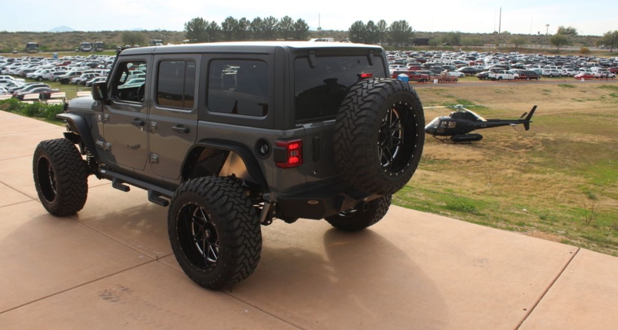 A lifted dark gray Jeep Wrangler with large black wheels and a spare tire parked on a concrete surface