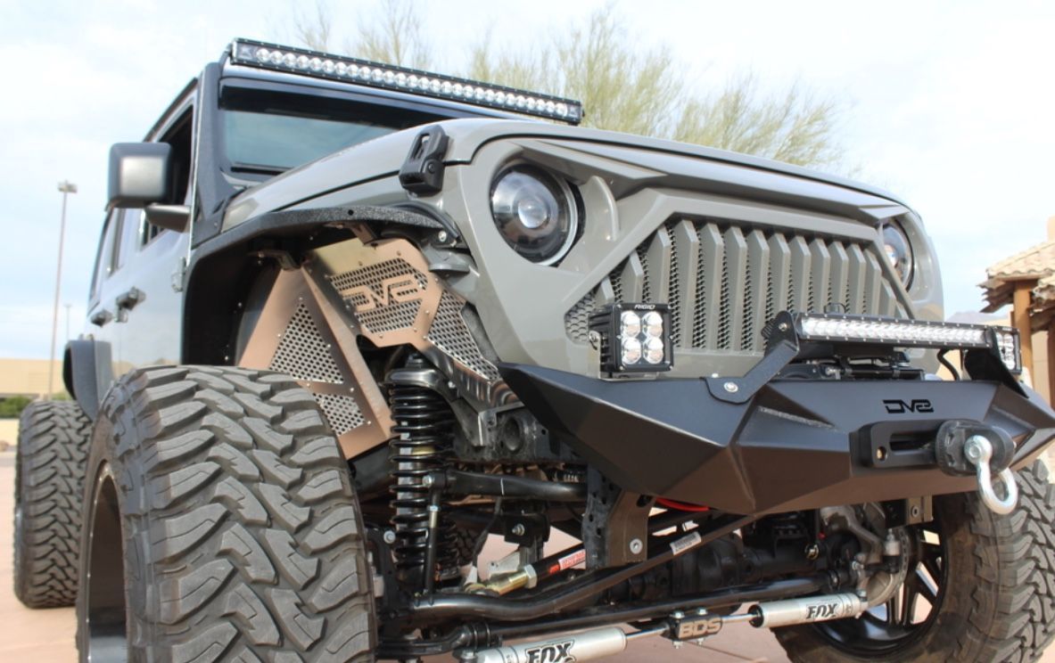Modified gray Jeep Wrangler with large off-road tires and custom front end.