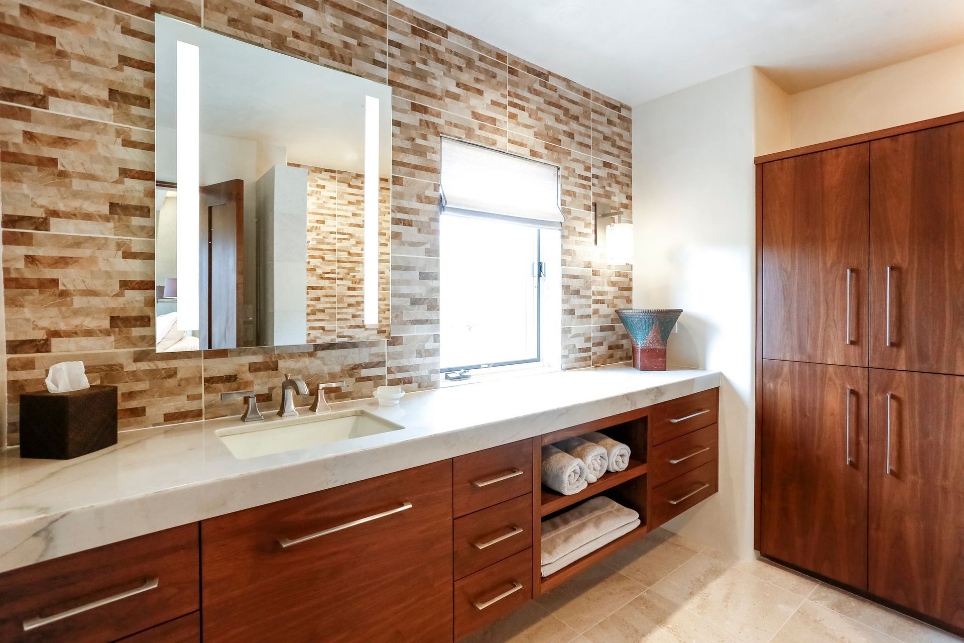 Modern bathroom with brick accent wall, walnut cabinetry, and lighted mirror.