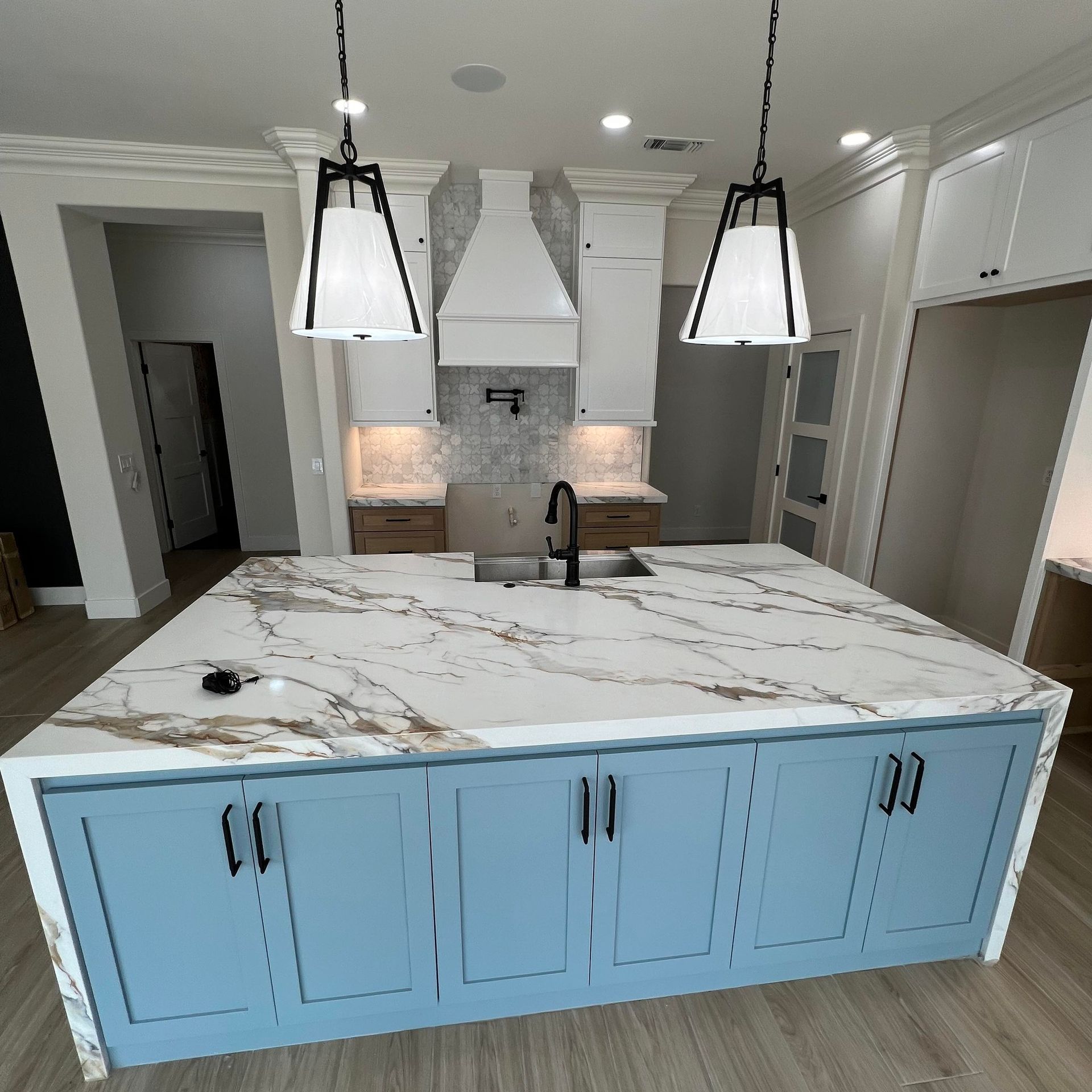 Blue kitchen island with marble countertop, white cabinets, and pendant lights.