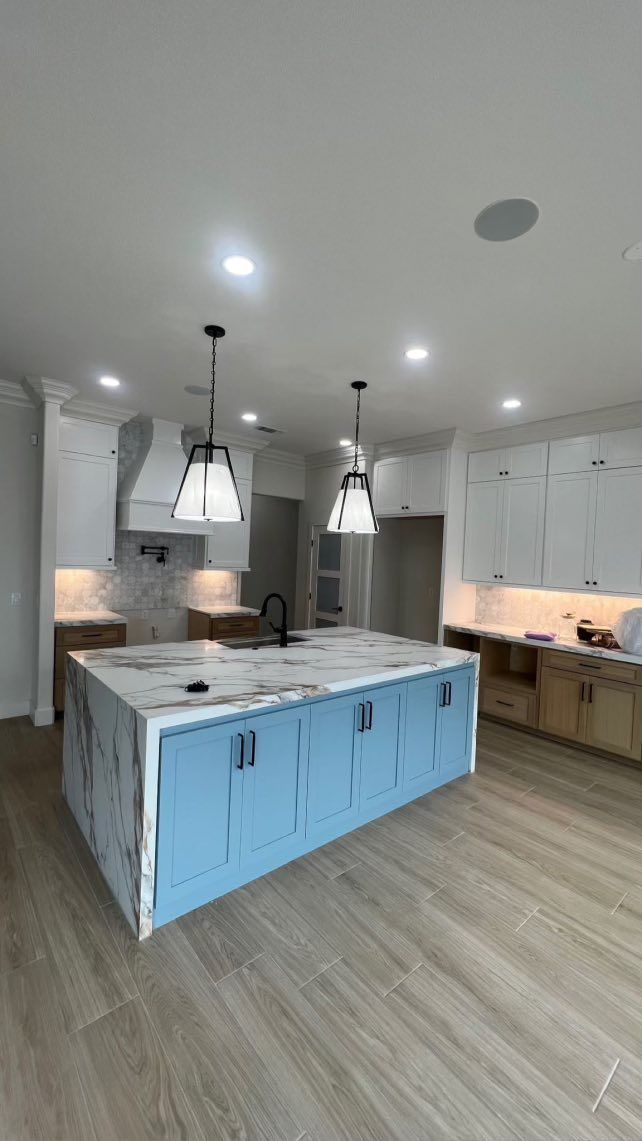 Blue kitchen island with white countertop, pendant lights, and light wood cabinets.