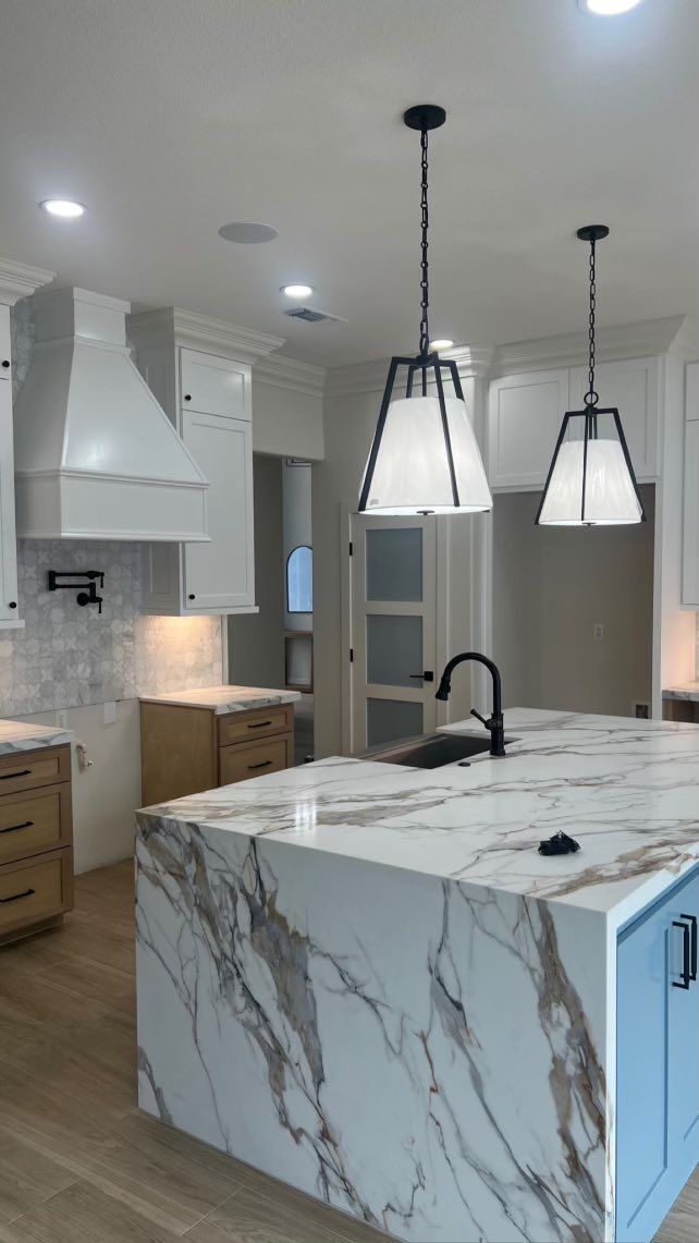 Kitchen with white cabinets, marble island, and black pendant lights.