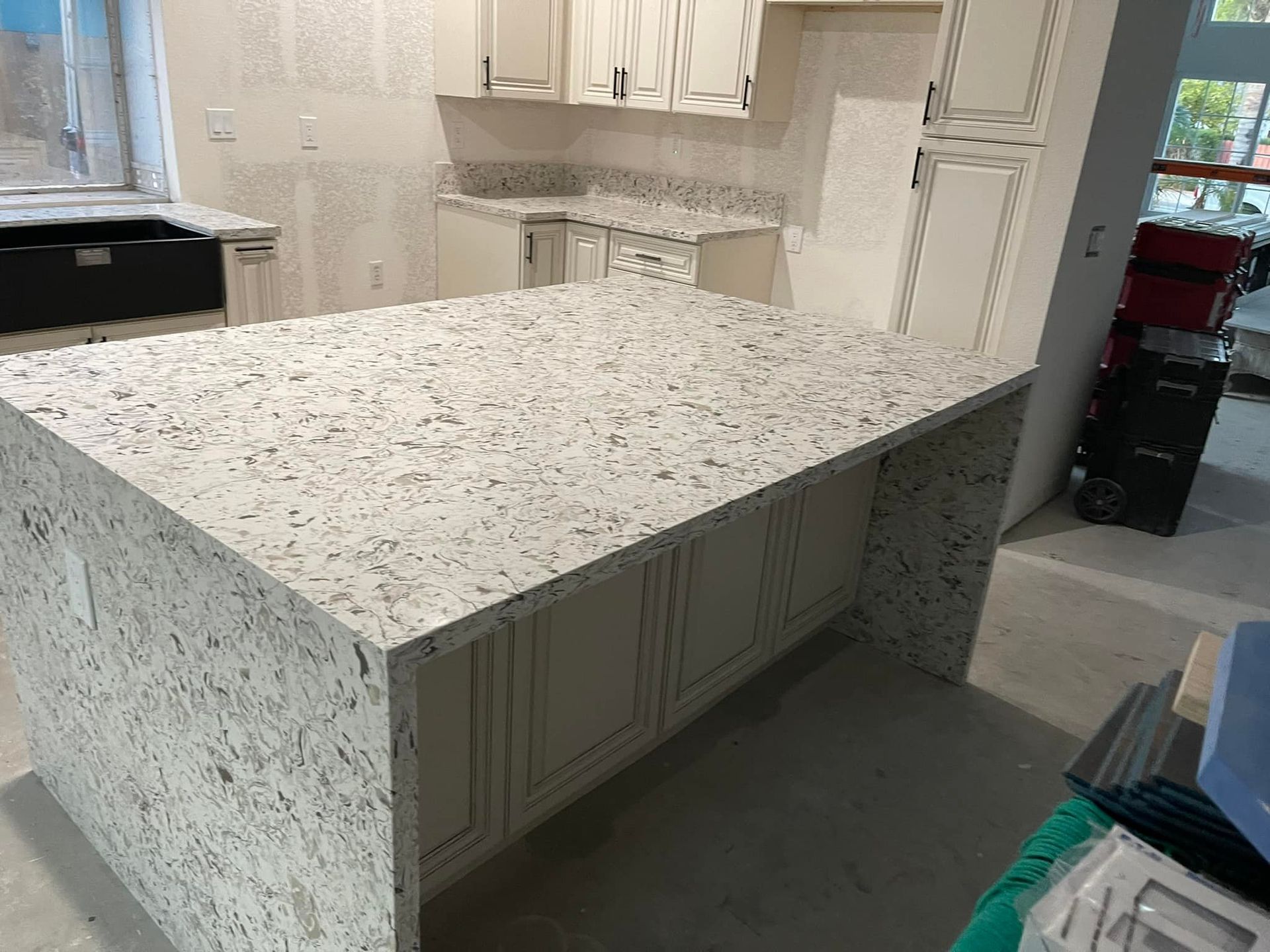 Kitchen with white cabinets, light-colored countertop island, and countertops against the wall.