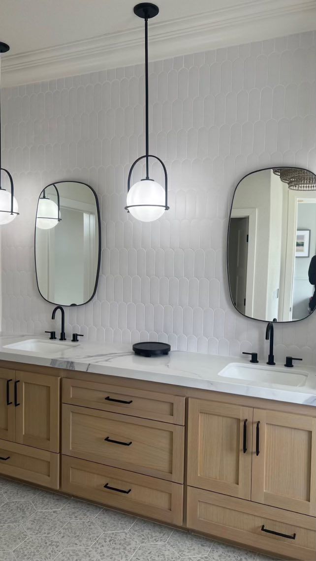Bathroom vanity with wood cabinets, white countertop, black fixtures, oval mirrors, and pendant lights.