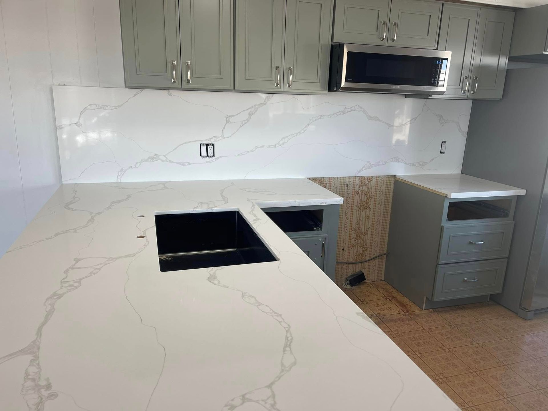 Gray kitchen with white quartz countertops, backsplash, and cabinets. A black sink is installed.
