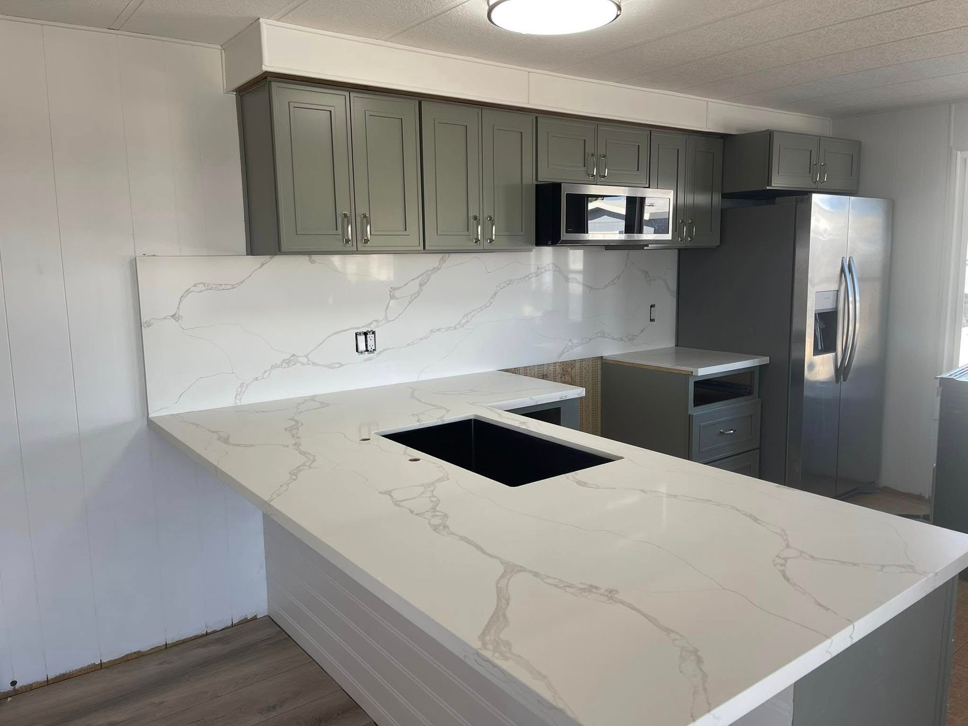 Kitchen remodel with white countertops, gray cabinets, and stainless steel appliances.