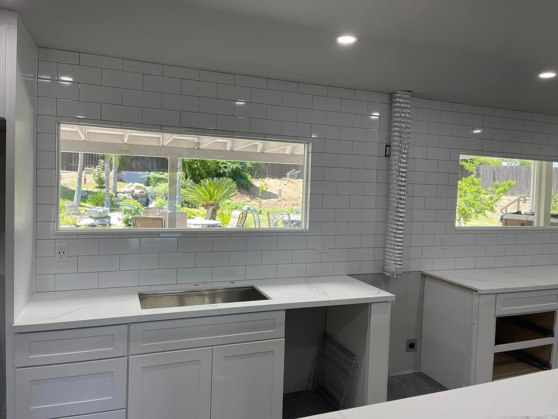 White kitchen with subway tile backsplash, countertops, and two windows overlooking greenery.