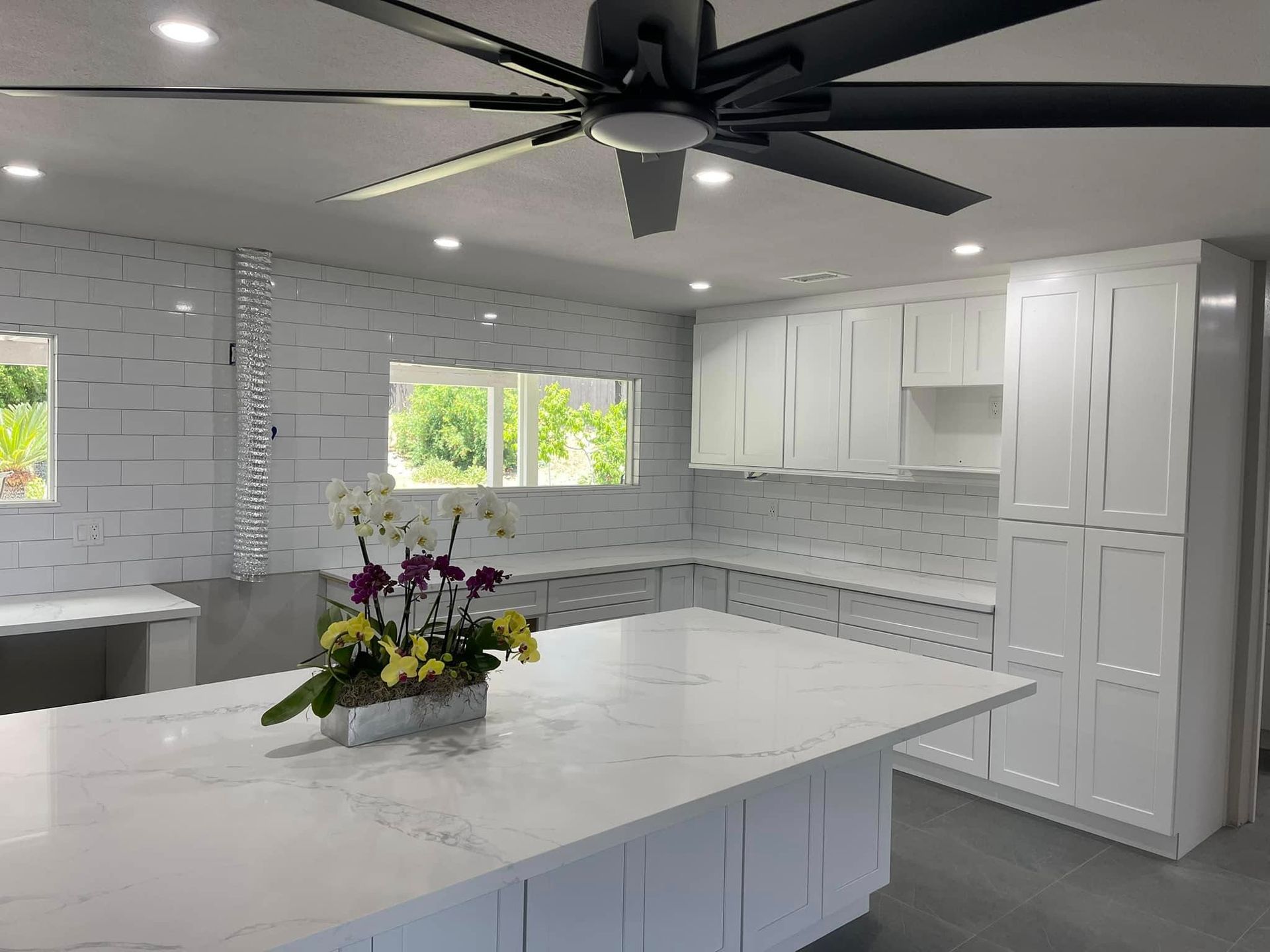 Kitchen island with granite countertop, sink, white cabinets, and a dishwasher, with a dining area in the background.
