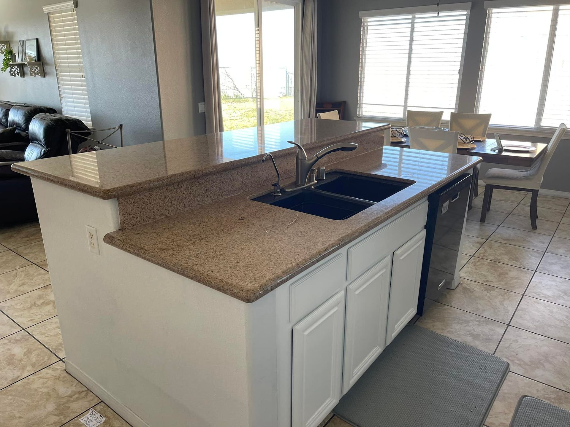Kitchen island with brown granite countertop, white cabinets, and a black sink.
