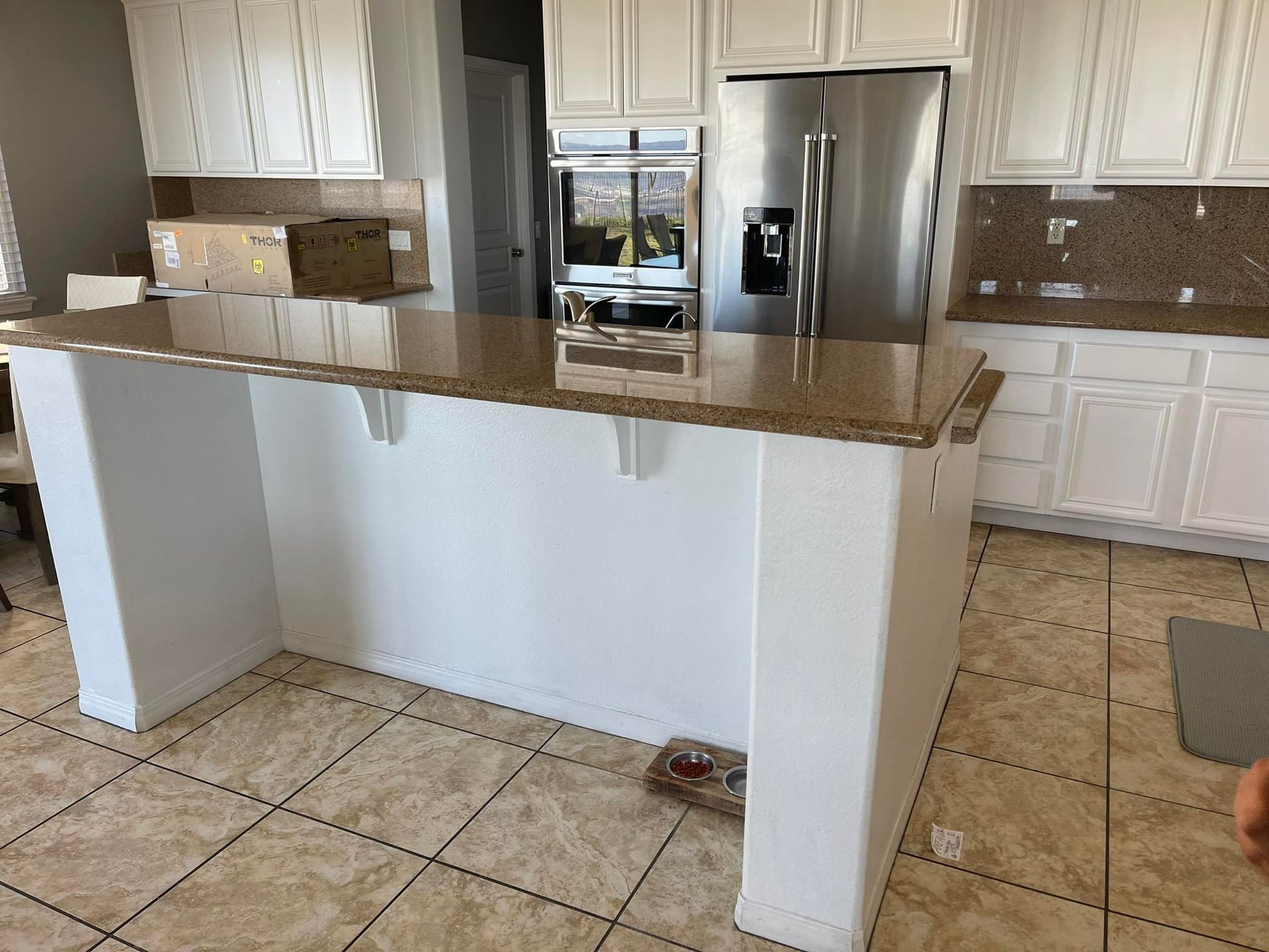 White kitchen island with a brown countertop, cabinets and stainless steel fridge.