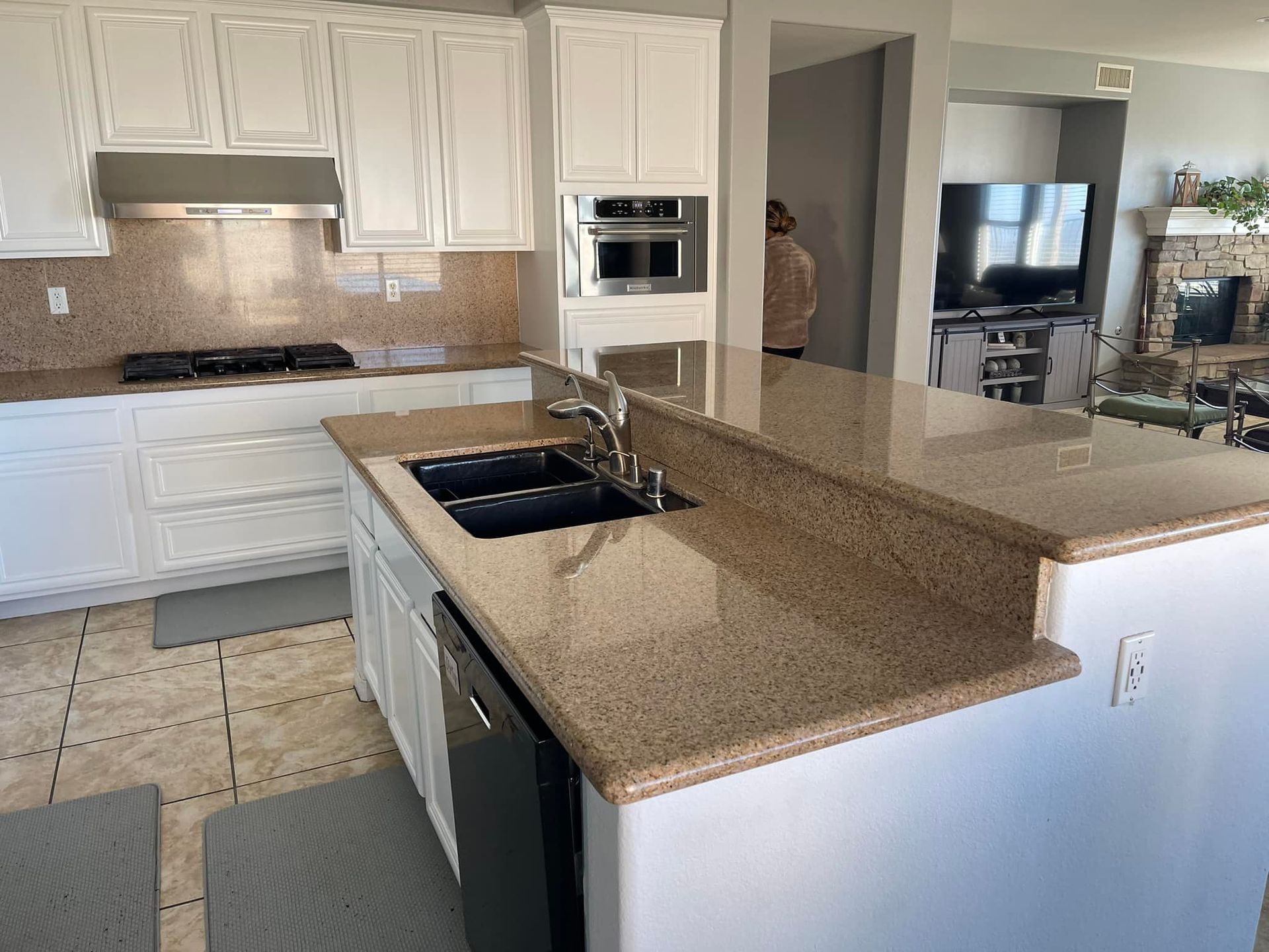 White kitchen with tan countertops, black appliances, and a person standing in the background.
