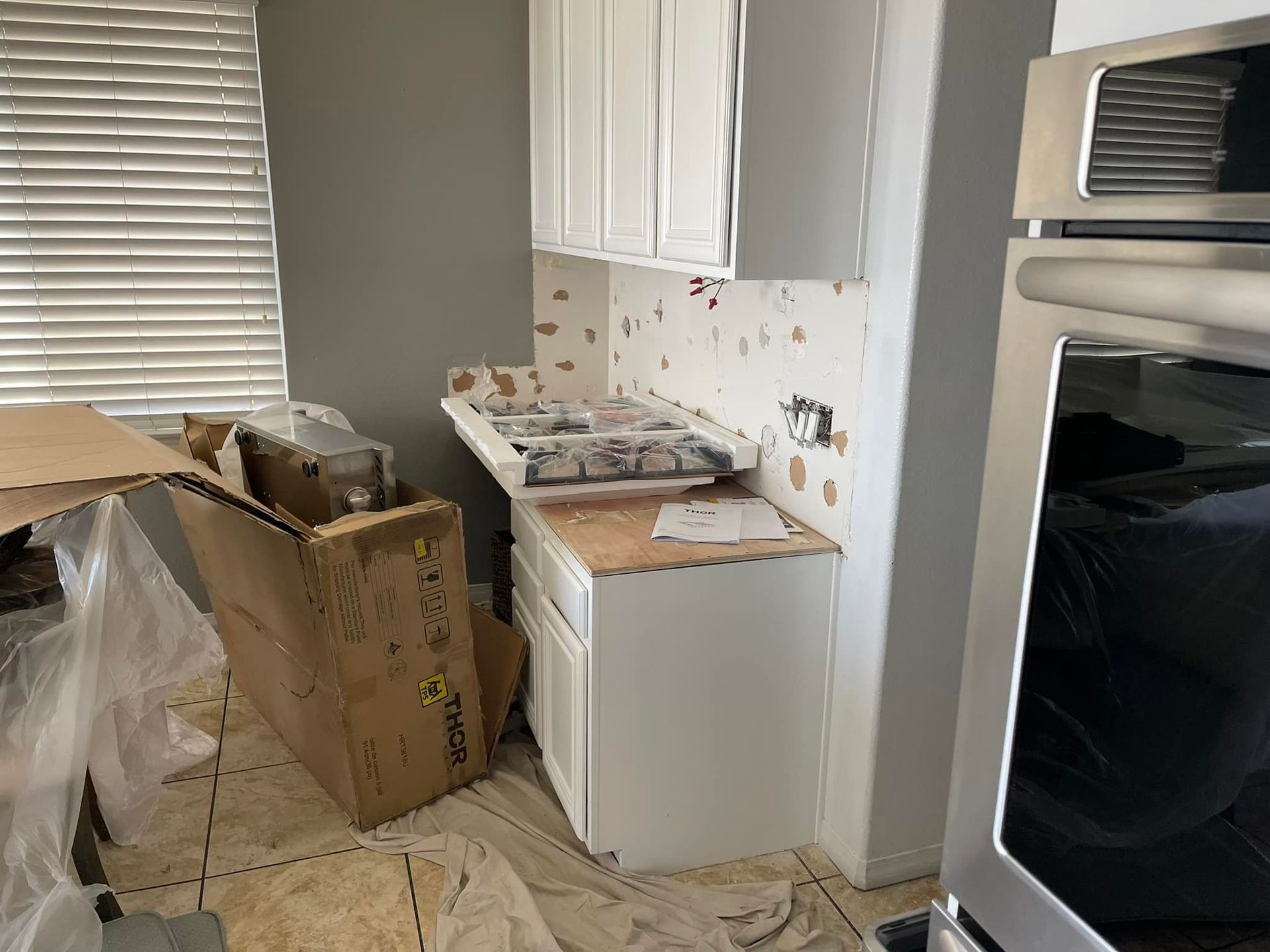 Kitchen under renovation. White cabinets, partially installed stove, boxes on the floor, and gray wall.