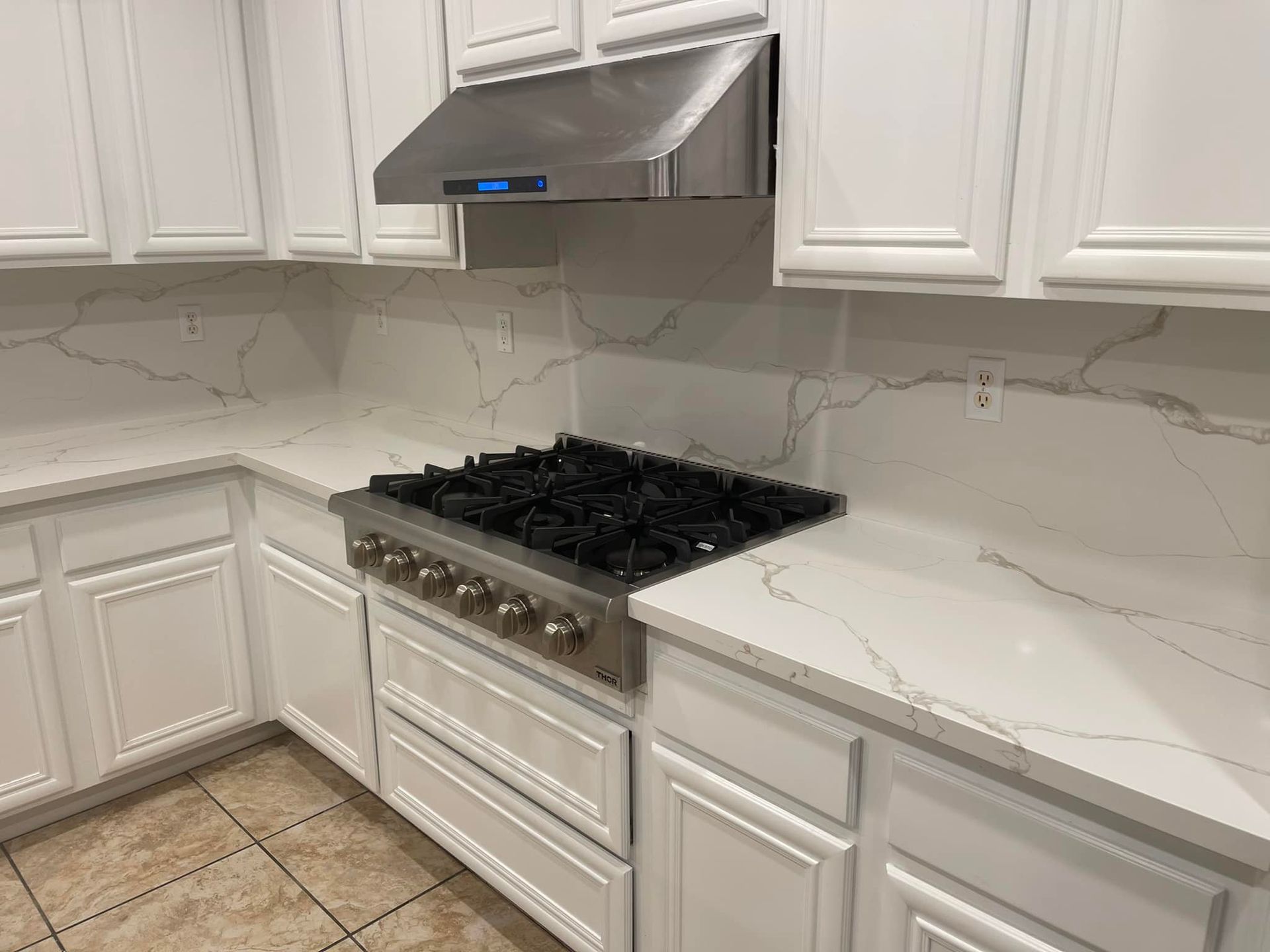 White kitchen with a gas range, stainless steel hood, and marble countertops.