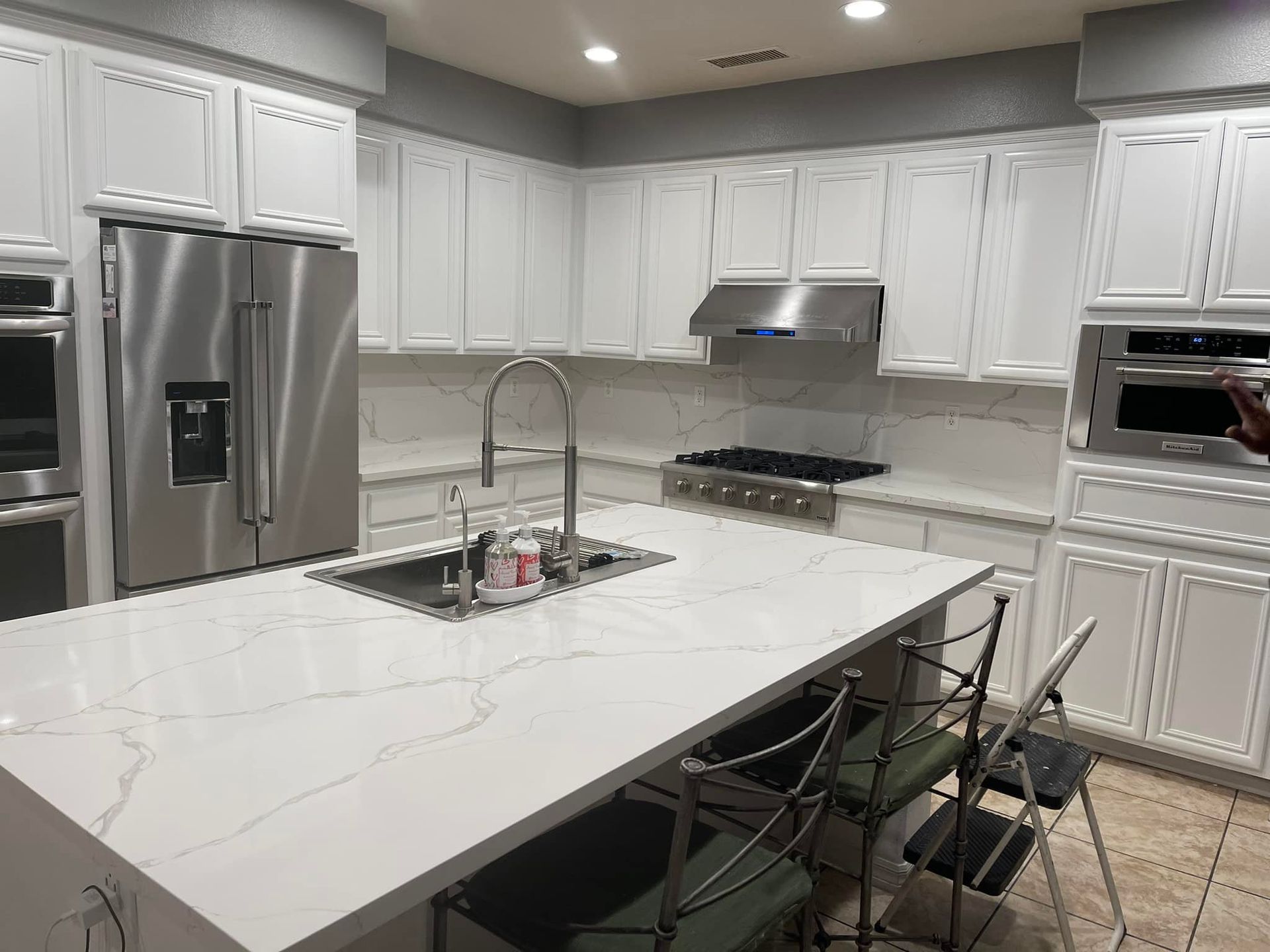 White kitchen with island, cabinets, stainless steel appliances, and marble countertops.
