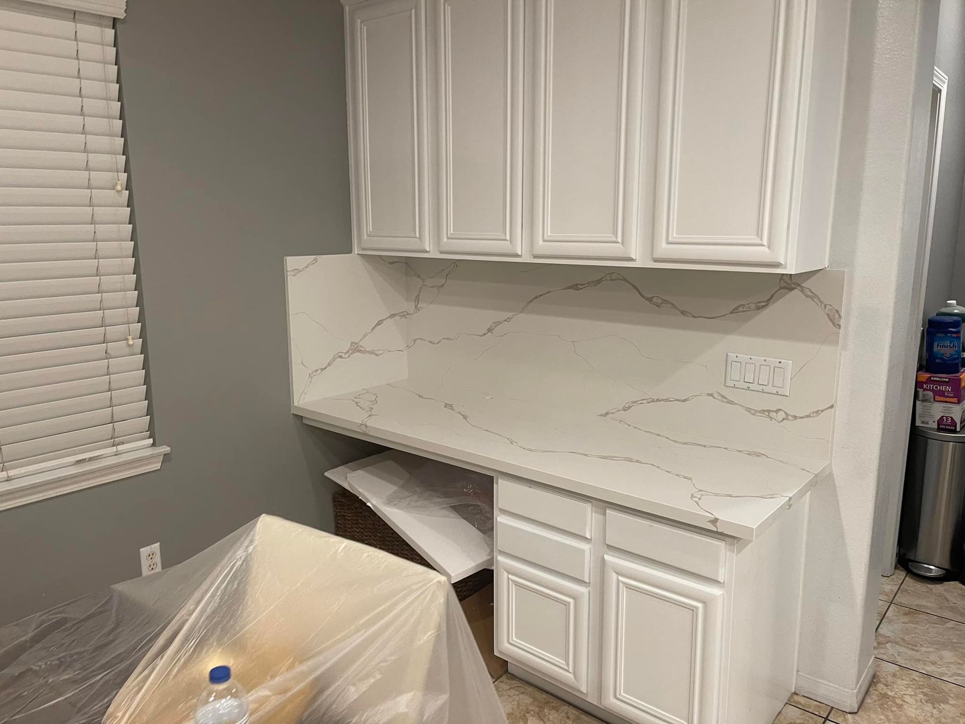 White desk and cabinets in a home with white countertops and a gray wall.