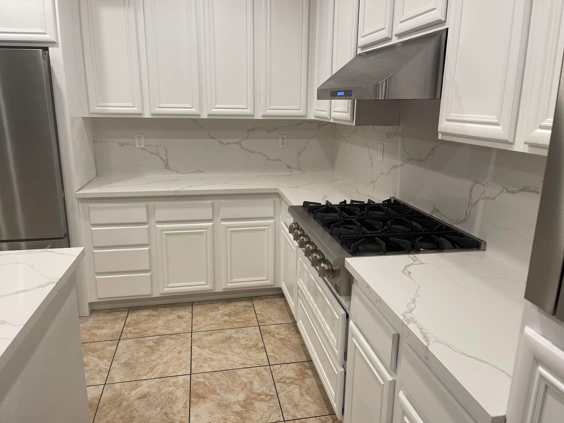 White kitchen with countertops, cabinets, stove, and tile floor.