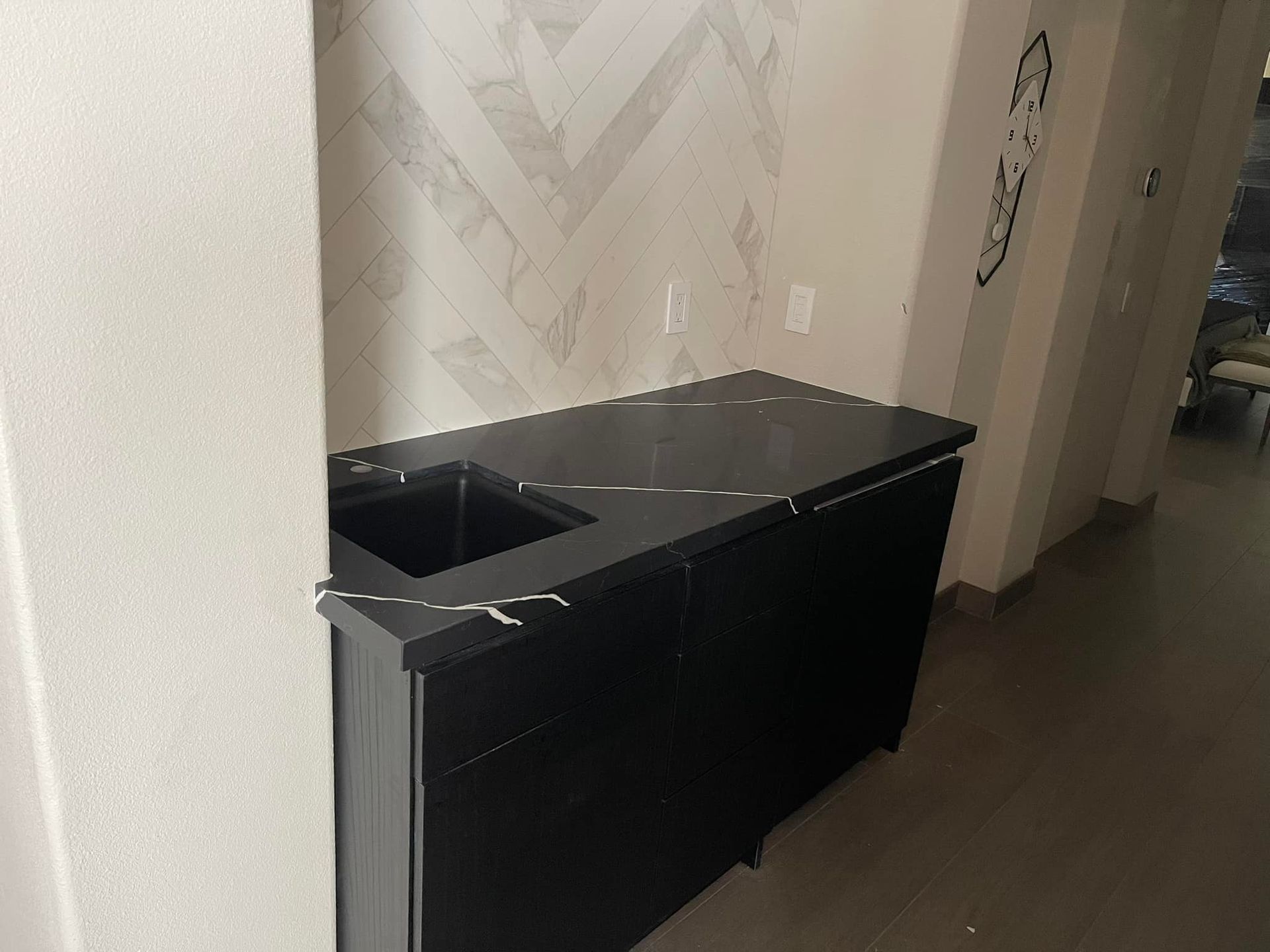 Black cabinet with black countertop and sink in a hallway, with a patterned wall.