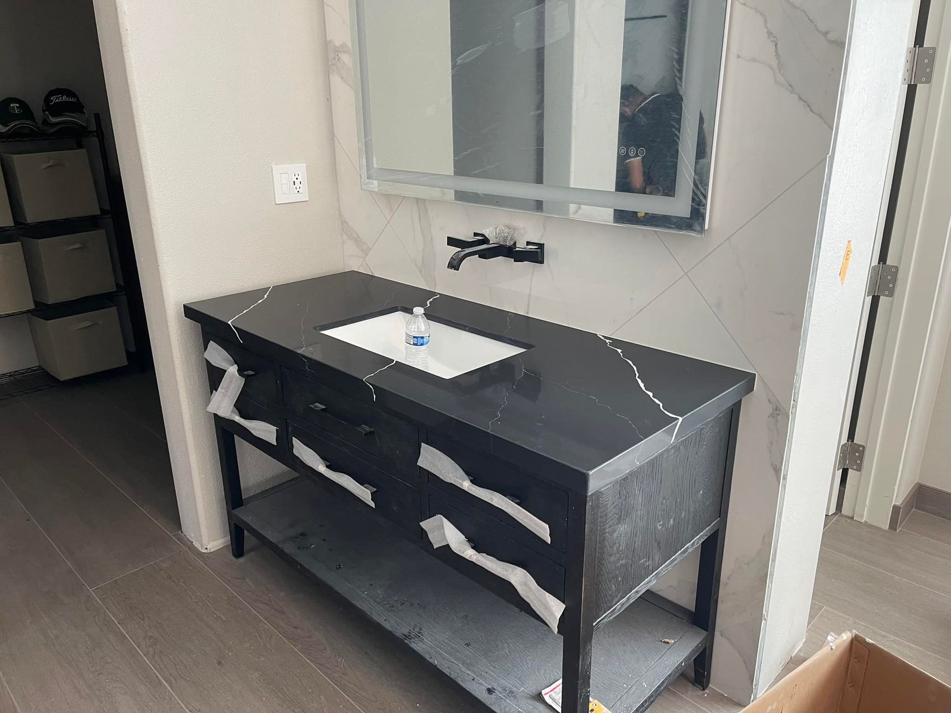 Bathroom with black vanity, white sink, mirror, and marble tile wall.