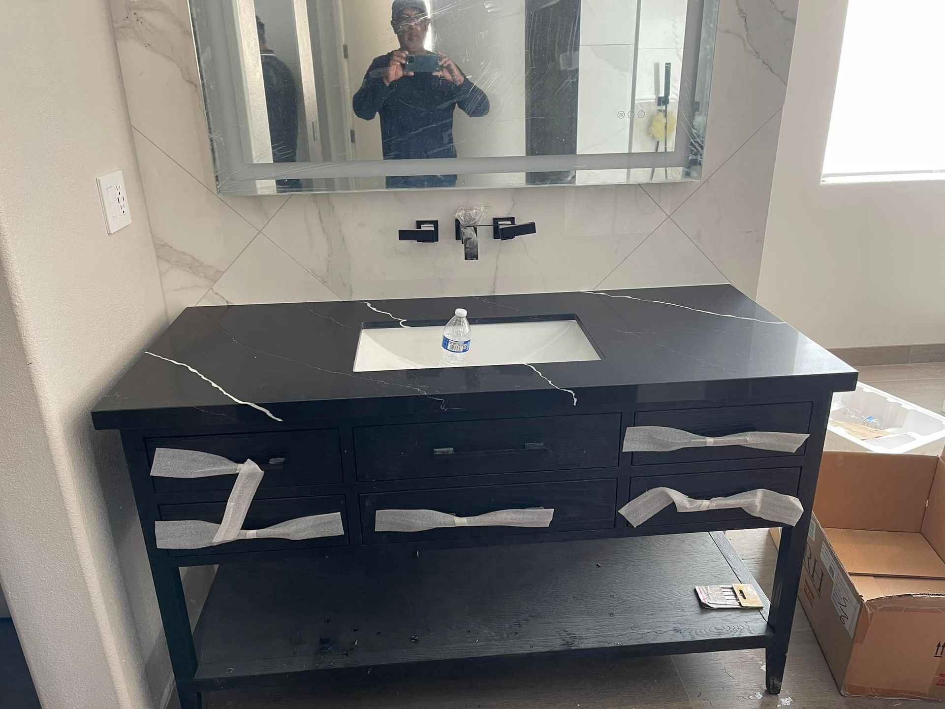 Bathroom vanity with a black countertop and dark wood cabinet. A mirror hangs above, and a person is visible.