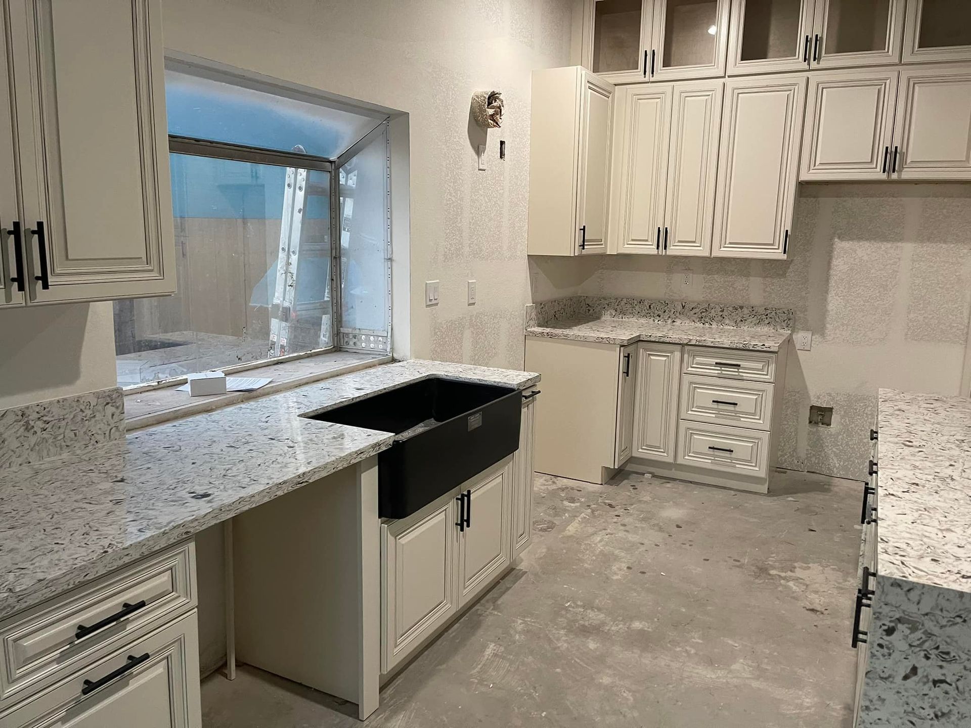 Kitchen under construction with white cabinets, granite countertops, and a large black sink.