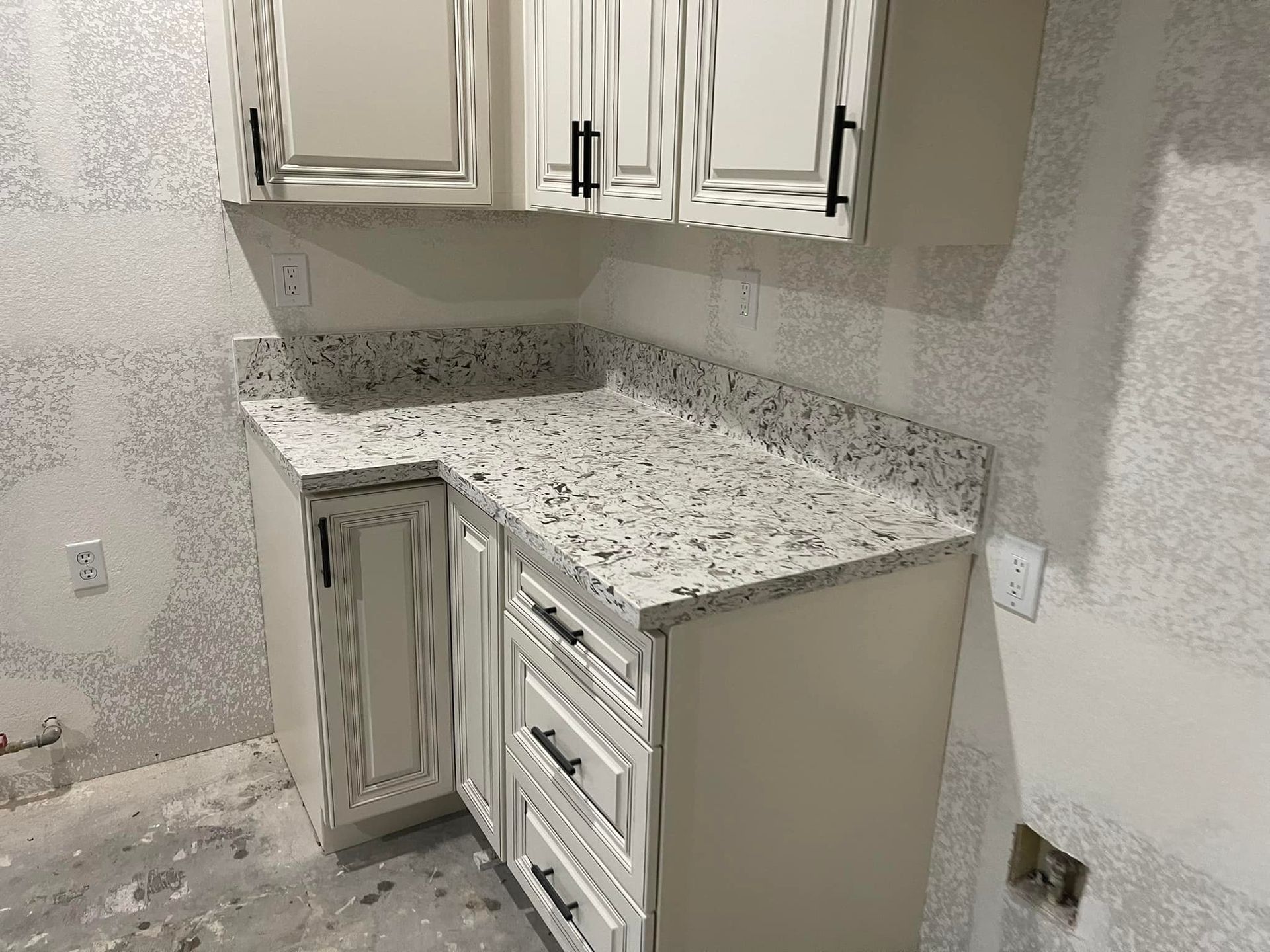Cream-colored kitchen cabinets with black handles, a granite countertop, and a gray wall.