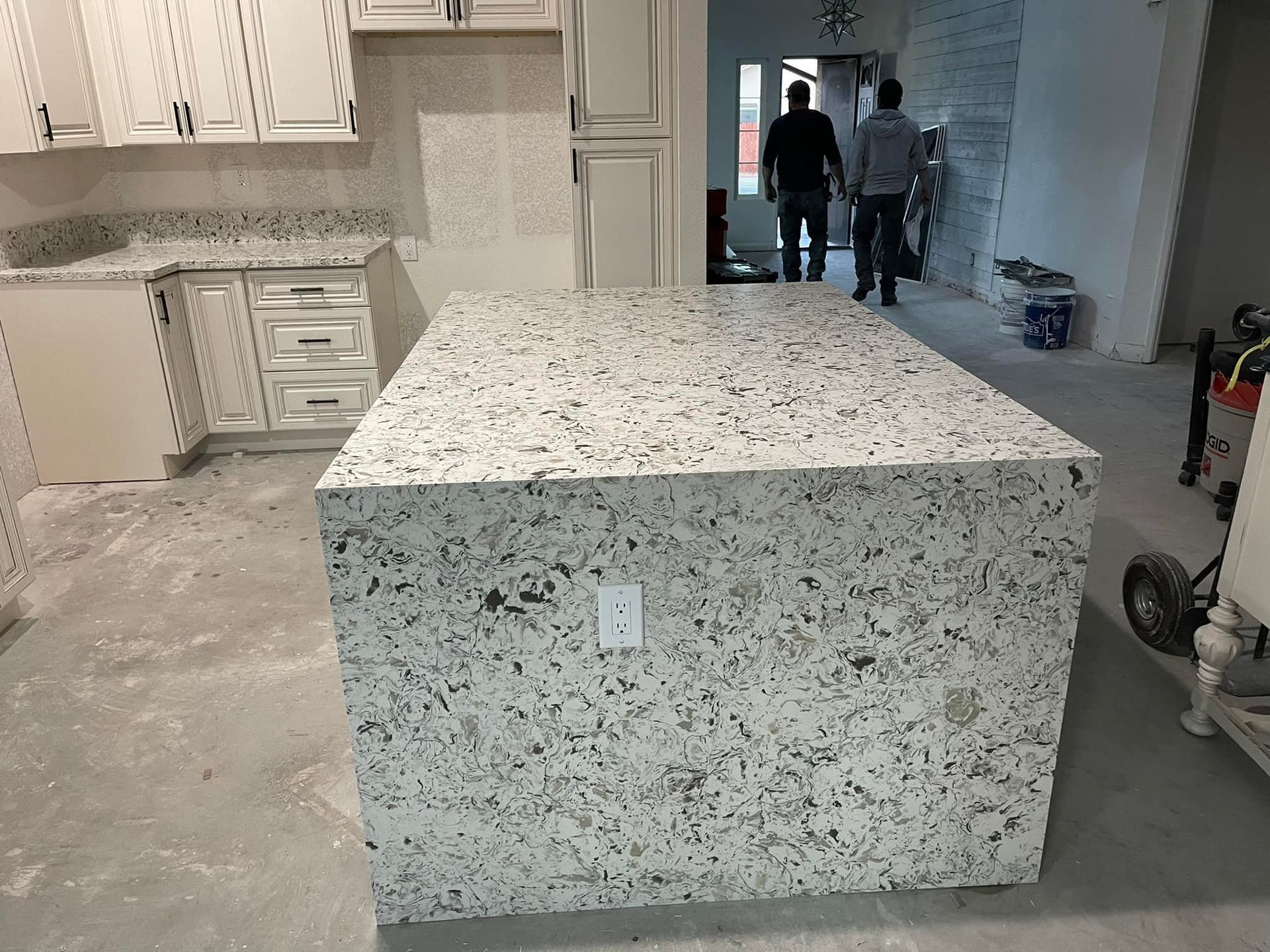 Kitchen with a large stone island, cabinets, and two men in the background.