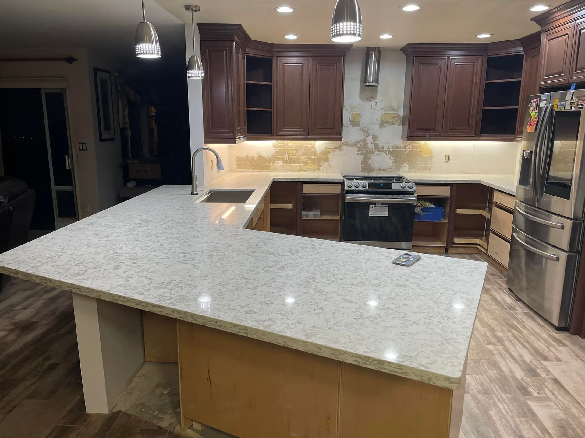 Kitchen remodel: light countertops, dark cabinets, partially installed cabinets and appliances, and exposed wall.