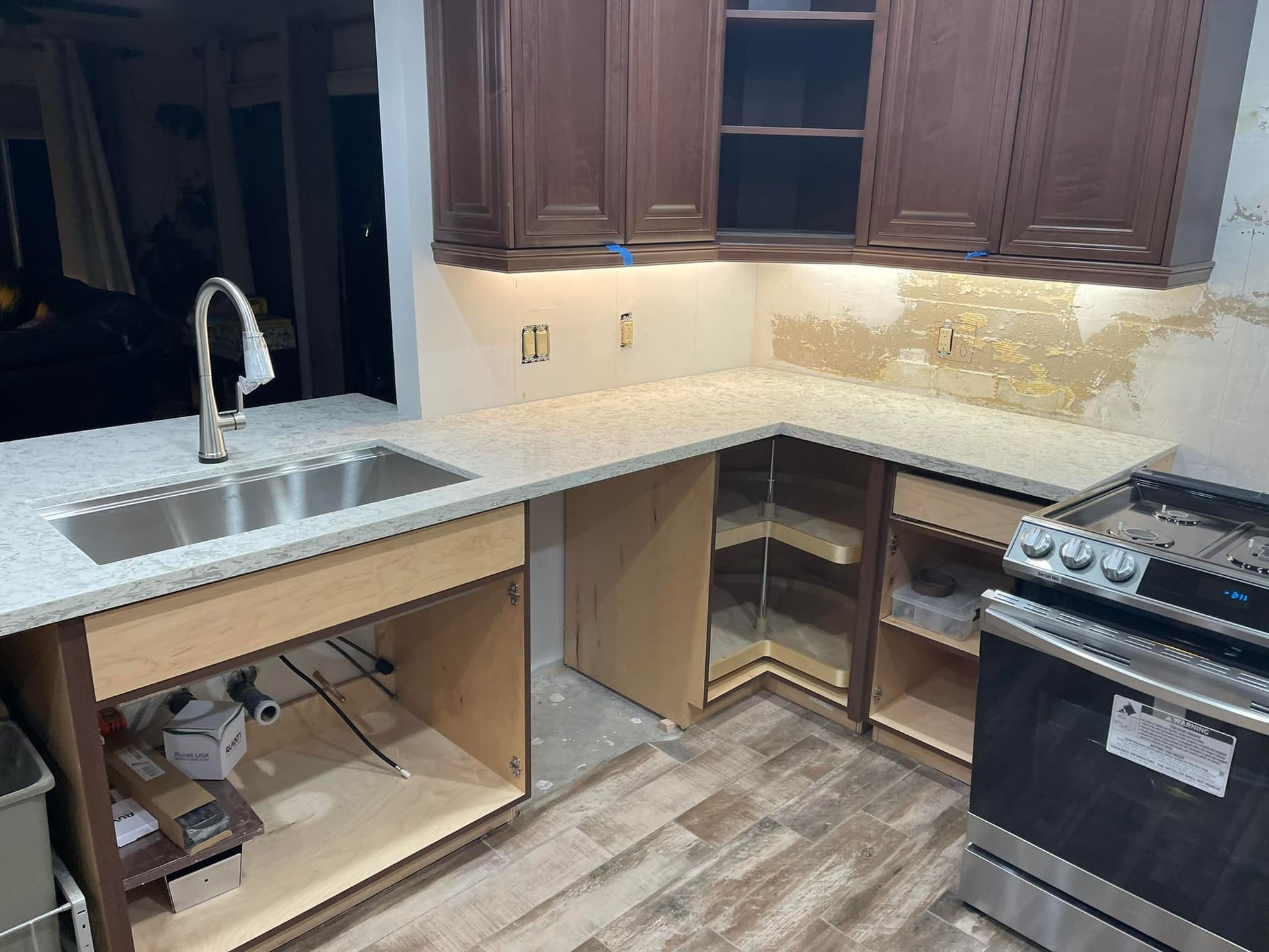Kitchen renovation in progress: brown cabinets, white countertop, stainless steel sink and appliances.
