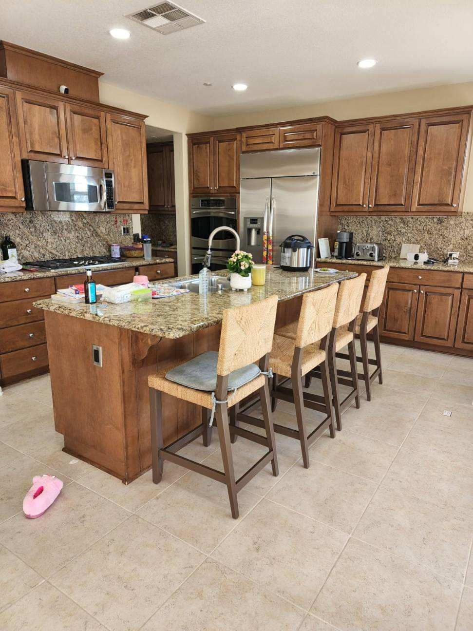 Kitchen with wooden cabinets, island with seating, stainless steel appliances, and tiled floor.