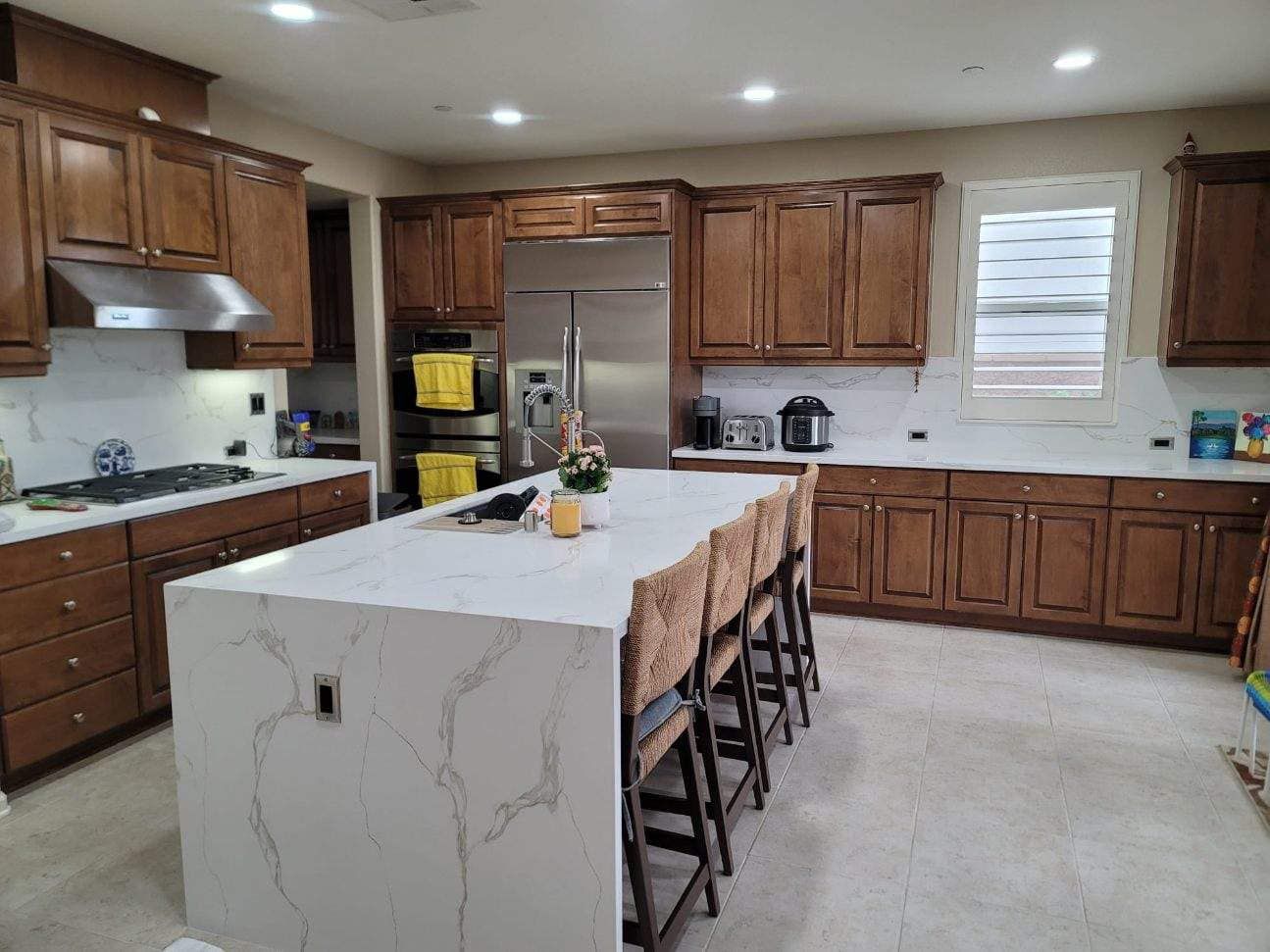 White kitchen cabinets with a countertop, a sink, and a window. Grey walls and a red fence can be seen.