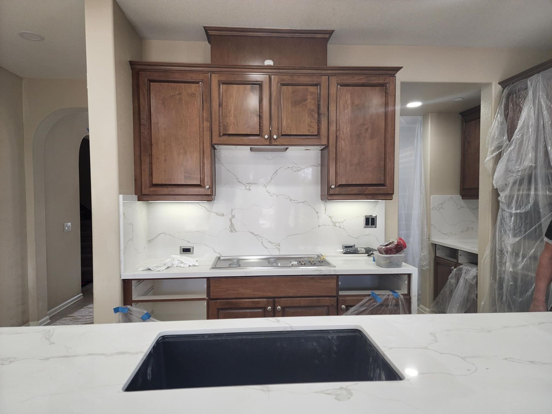 Kitchen with brown cabinets, marble backsplash, and white countertops. Sink in foreground.