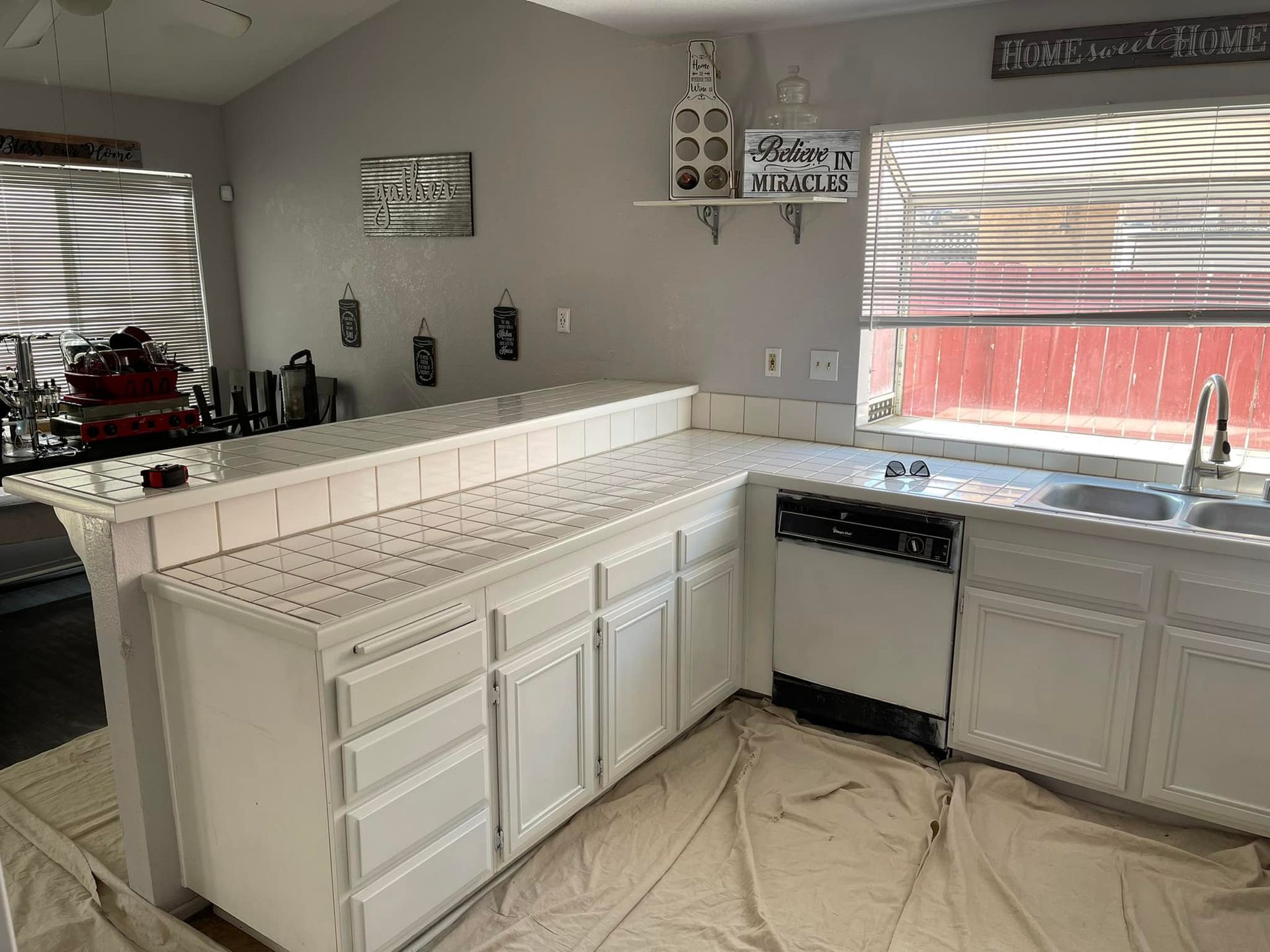 White kitchen cabinets and countertop with gray walls, a window, and appliances.
