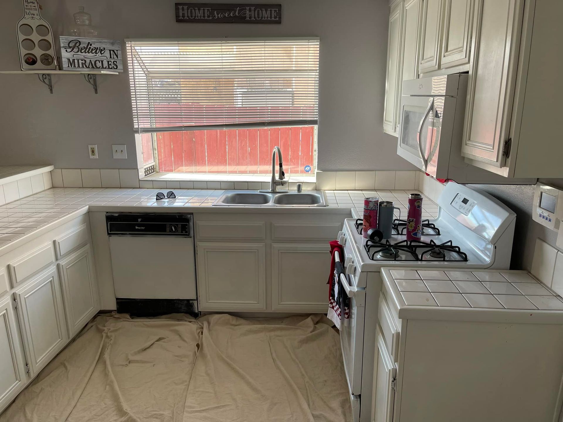 White kitchen with a sink, oven, and cabinets; tan drop cloths on the floor.