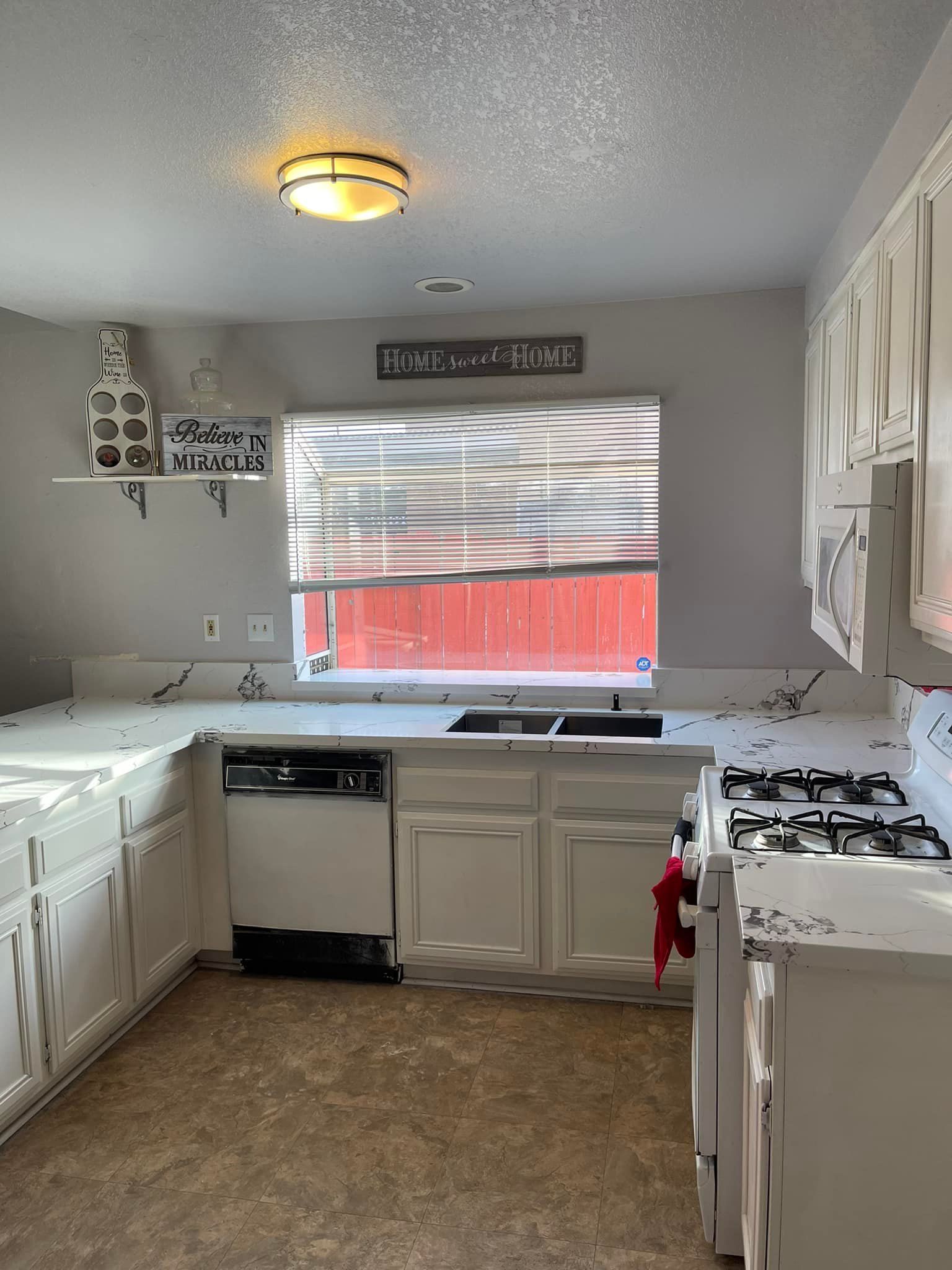 Kitchen with white cabinets, appliances, and counters. A window above a sink is visible.