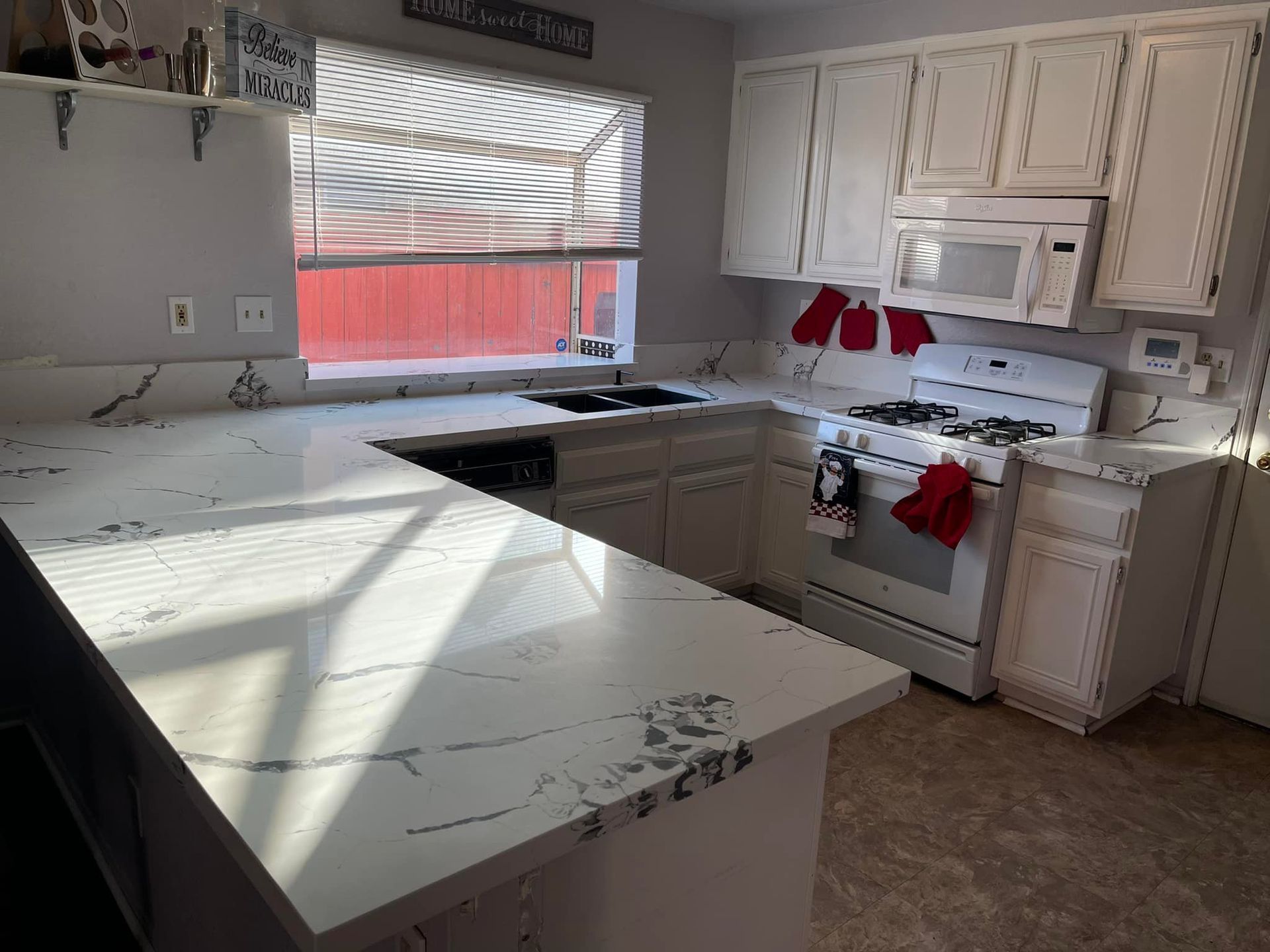 Kitchen with white cabinets, countertops, and appliances; sunlight streams through window.