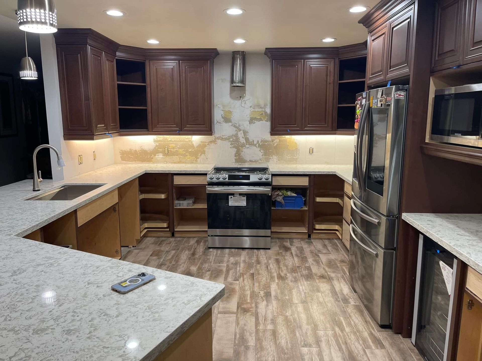 Kitchen undergoing renovation: brown cabinets, stainless steel appliances, beige walls, new countertops, and exposed cabinet frames.