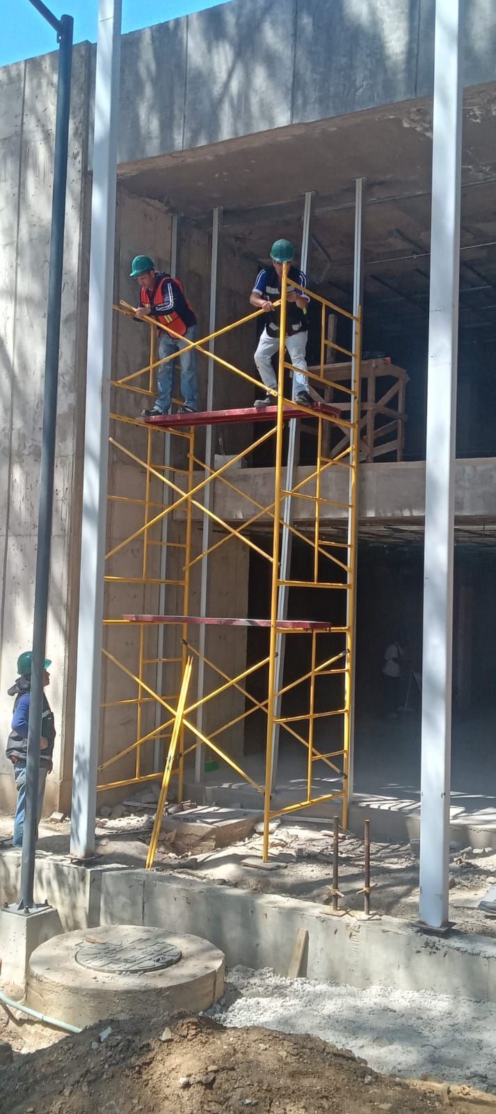 Obreros de la construcción sobre un andamio amarillo, trabajando en una obra.