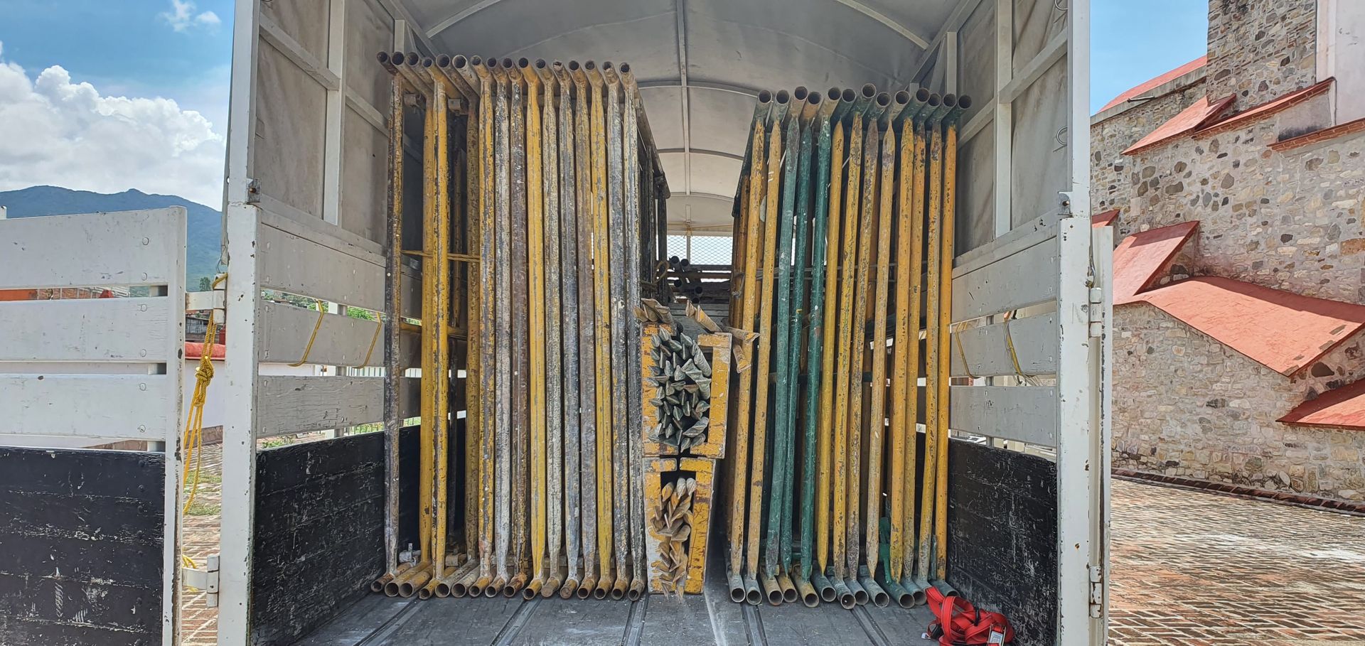 Andamios apilados dentro de un camión, con un edificio visible a la derecha.