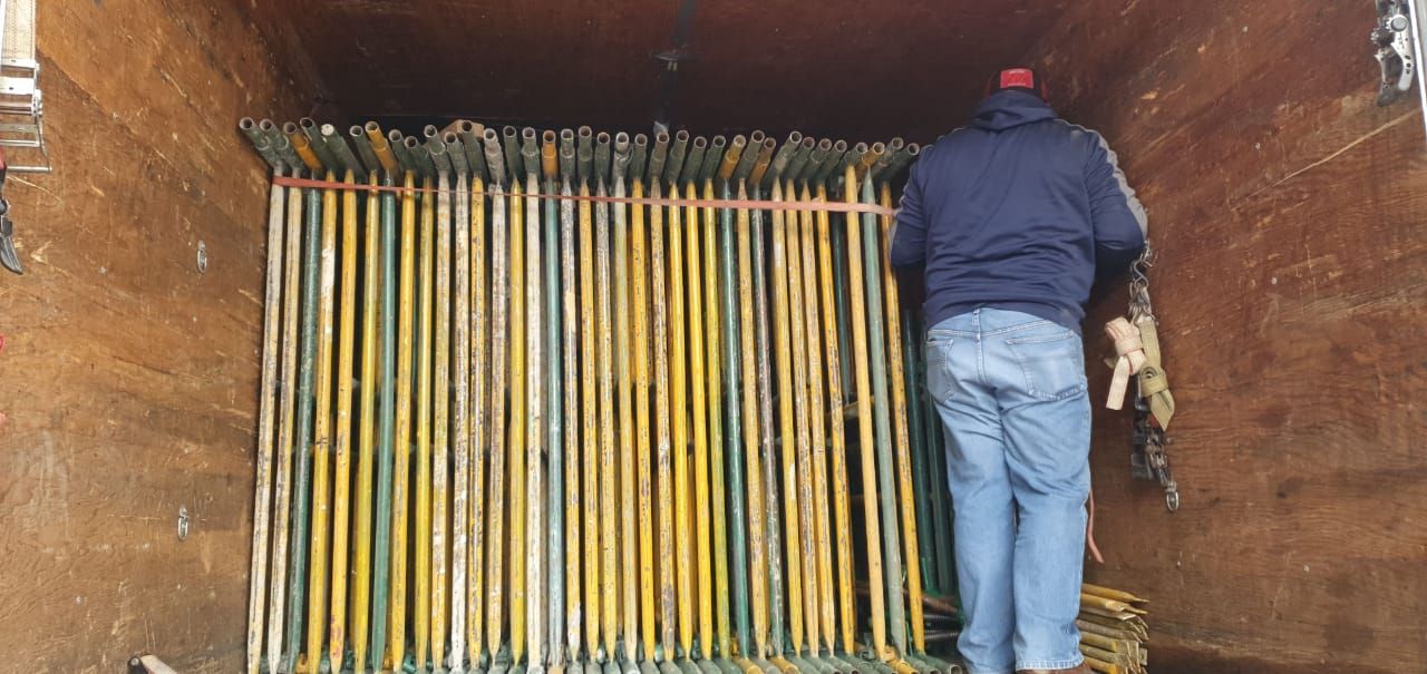 Una persona de pie dentro de un camión lleno de postes largos, amarillos y verdes.