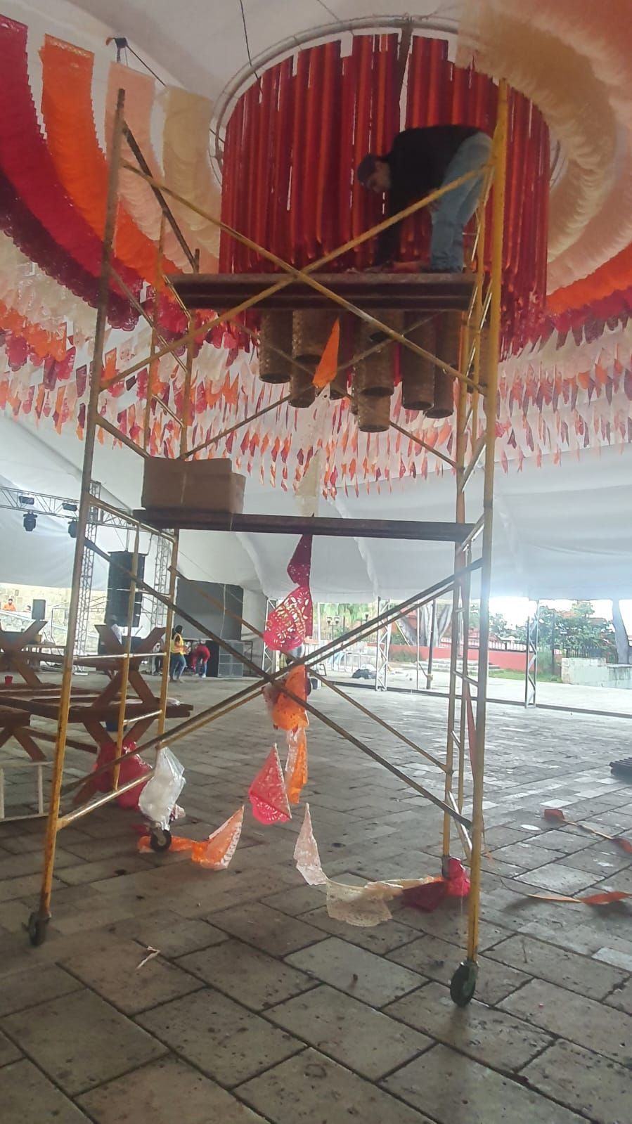 Una persona trabaja en una plataforma de andamio, colgando decoraciones de un techo cubierto de coloridas serpentinas de tela.