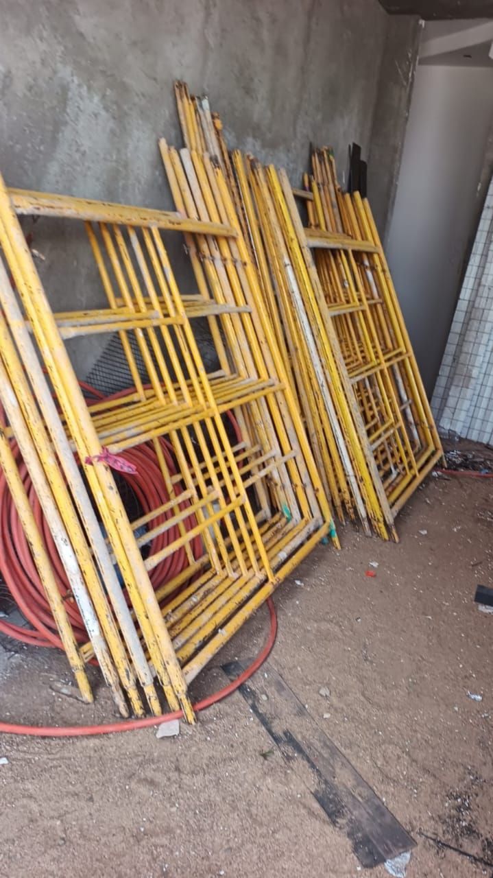 Estructuras de andamio amarillas apoyadas contra una pared, con una manguera roja y otros materiales de construcción a la vista.