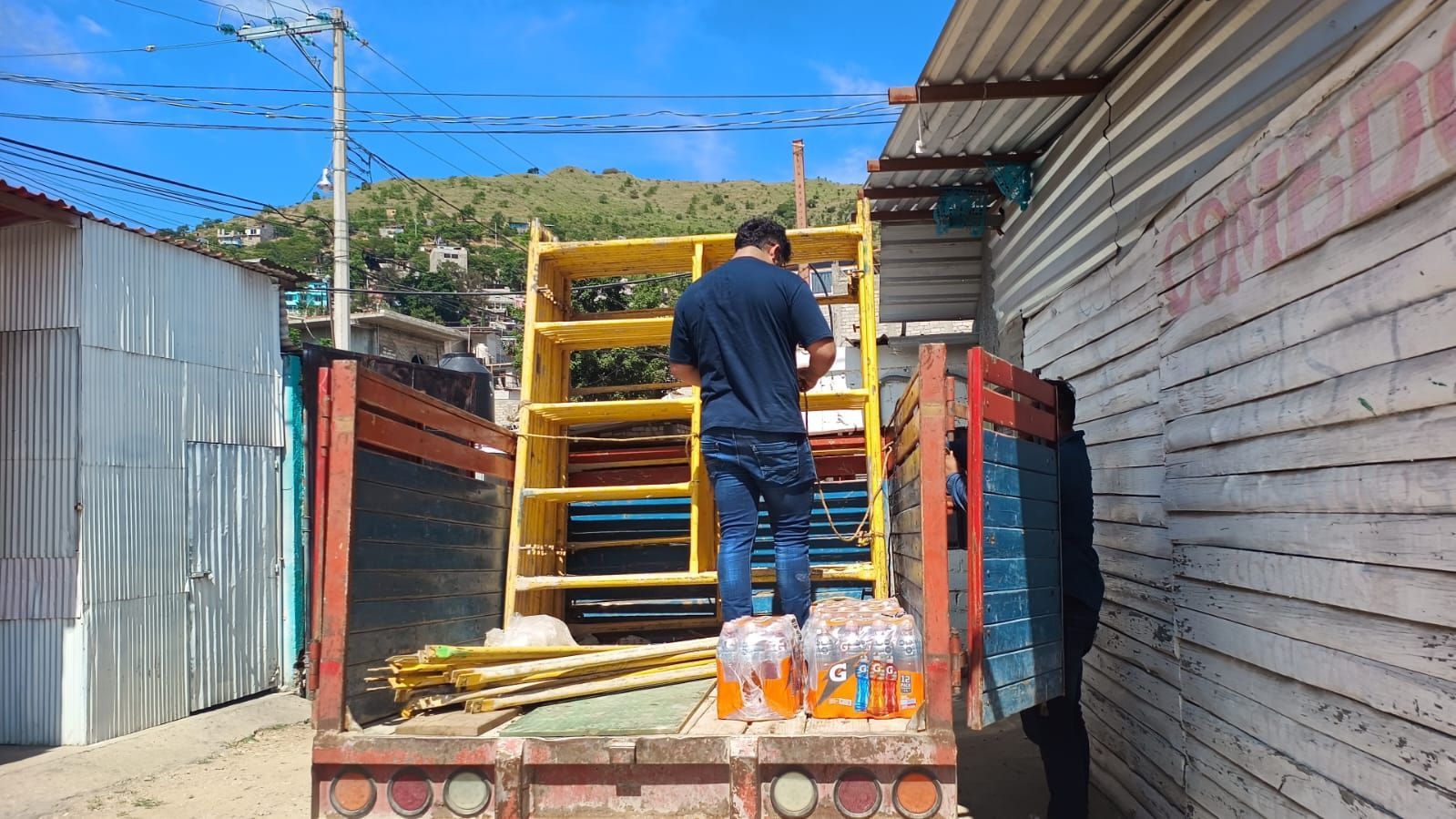 Hombre cargando un andamio amarillo en un camión, otra persona cerca, escena callejera.