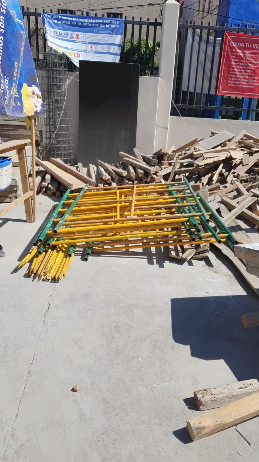 Andamios metálicos amarillos y tablones de madera se apilan sobre una superficie de hormigón en el exterior.
