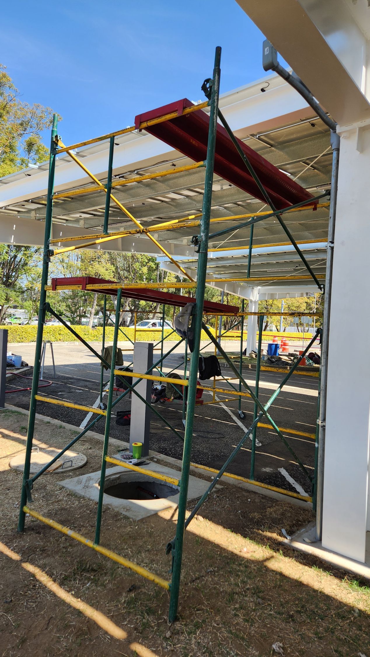 Andamios junto a un edificio en construcción; estructura metálica verde con plataformas rojas.